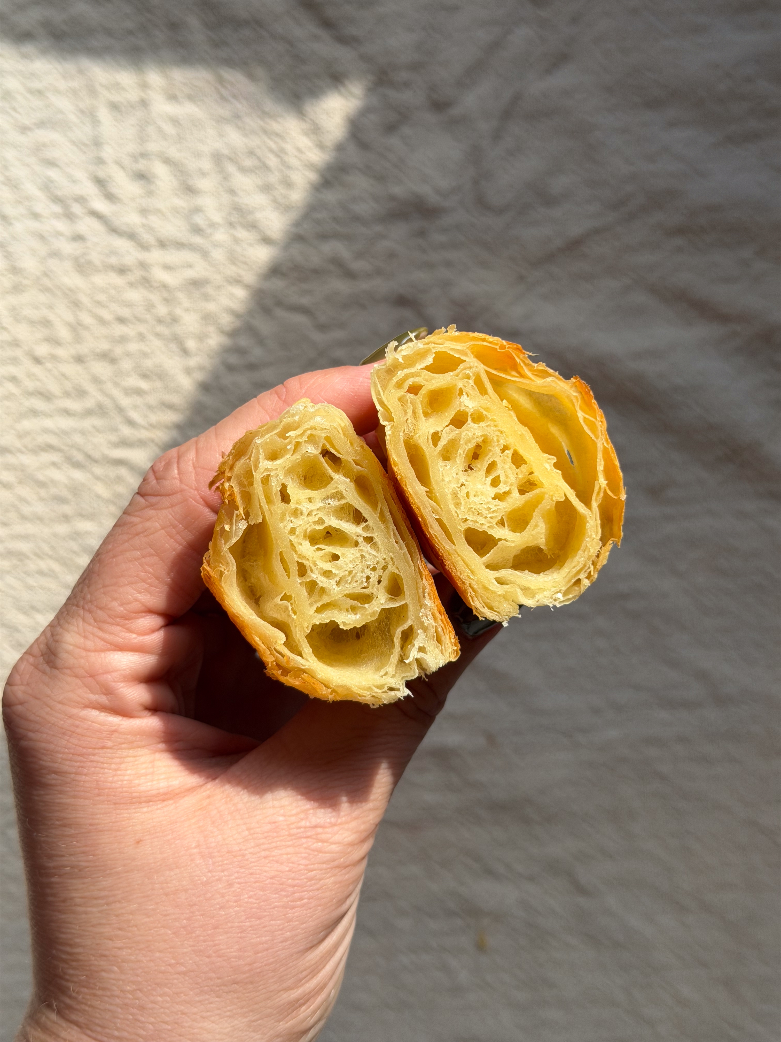 Hand holds a croissant cut in half, showing its flaky, airy layers against a neutral background