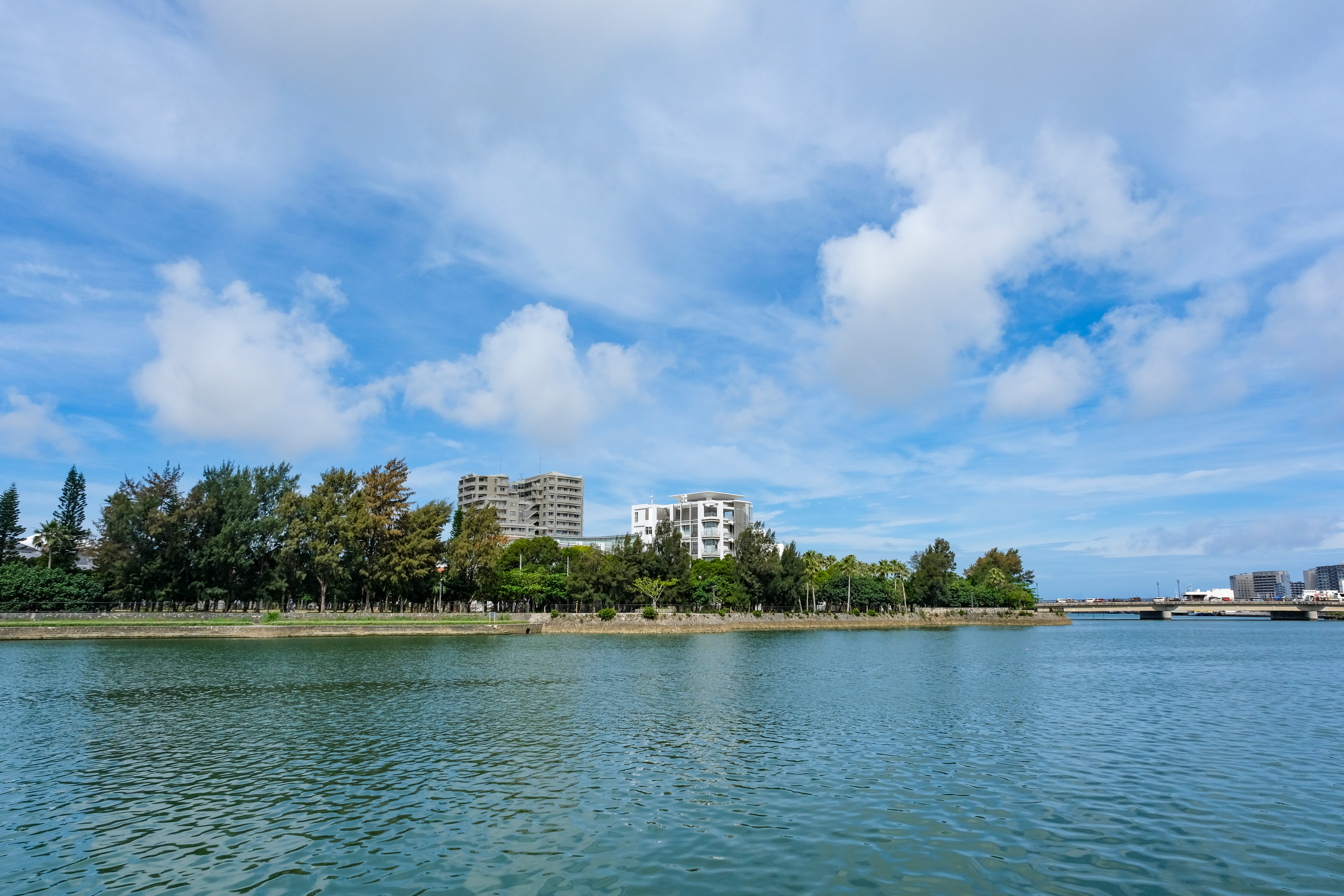 Scenic view of calm water with distant buildings and trees under a partly cloudy sky