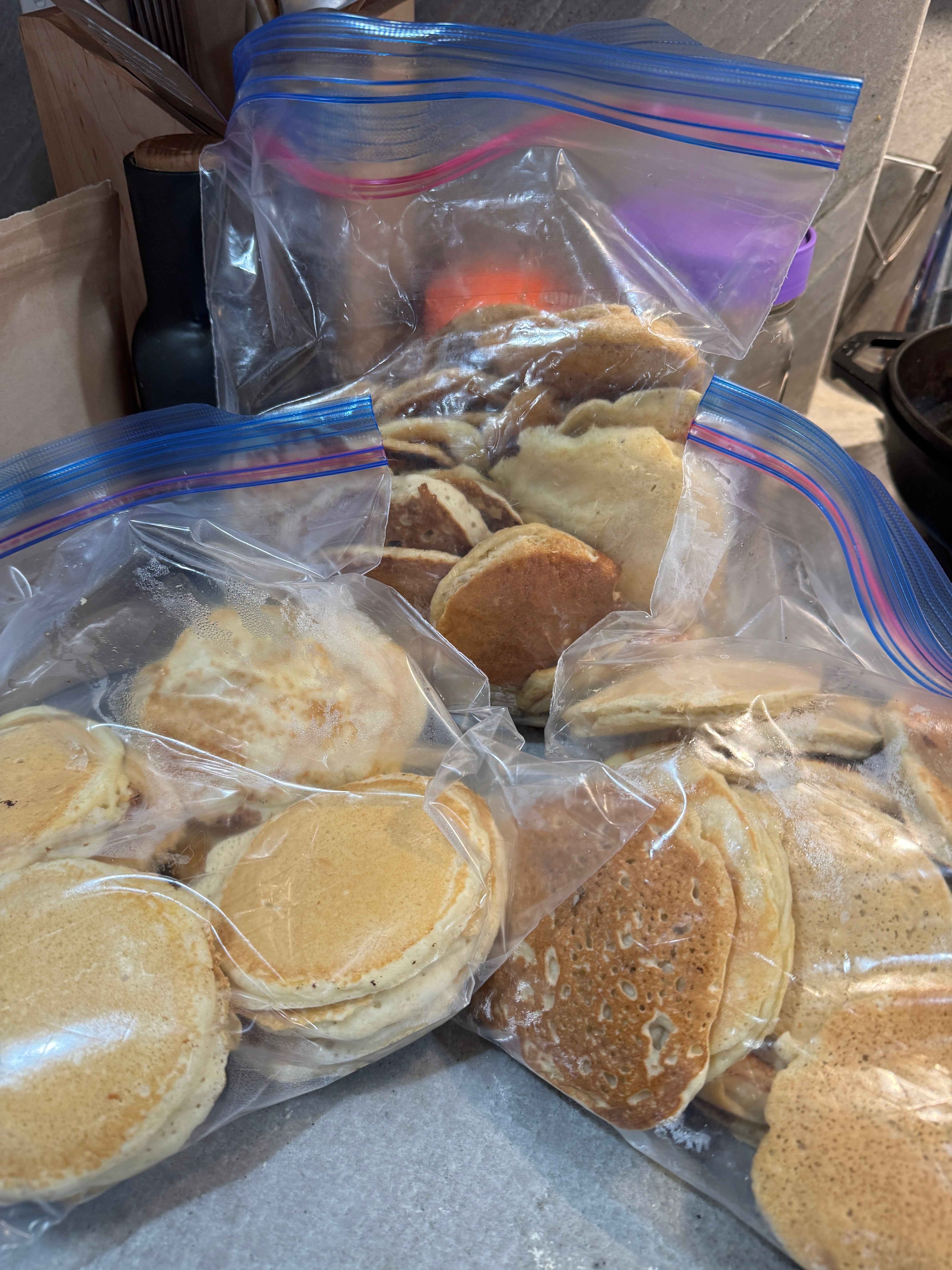 Plastic bags filled with homemade pancakes are stacked on a kitchen counter