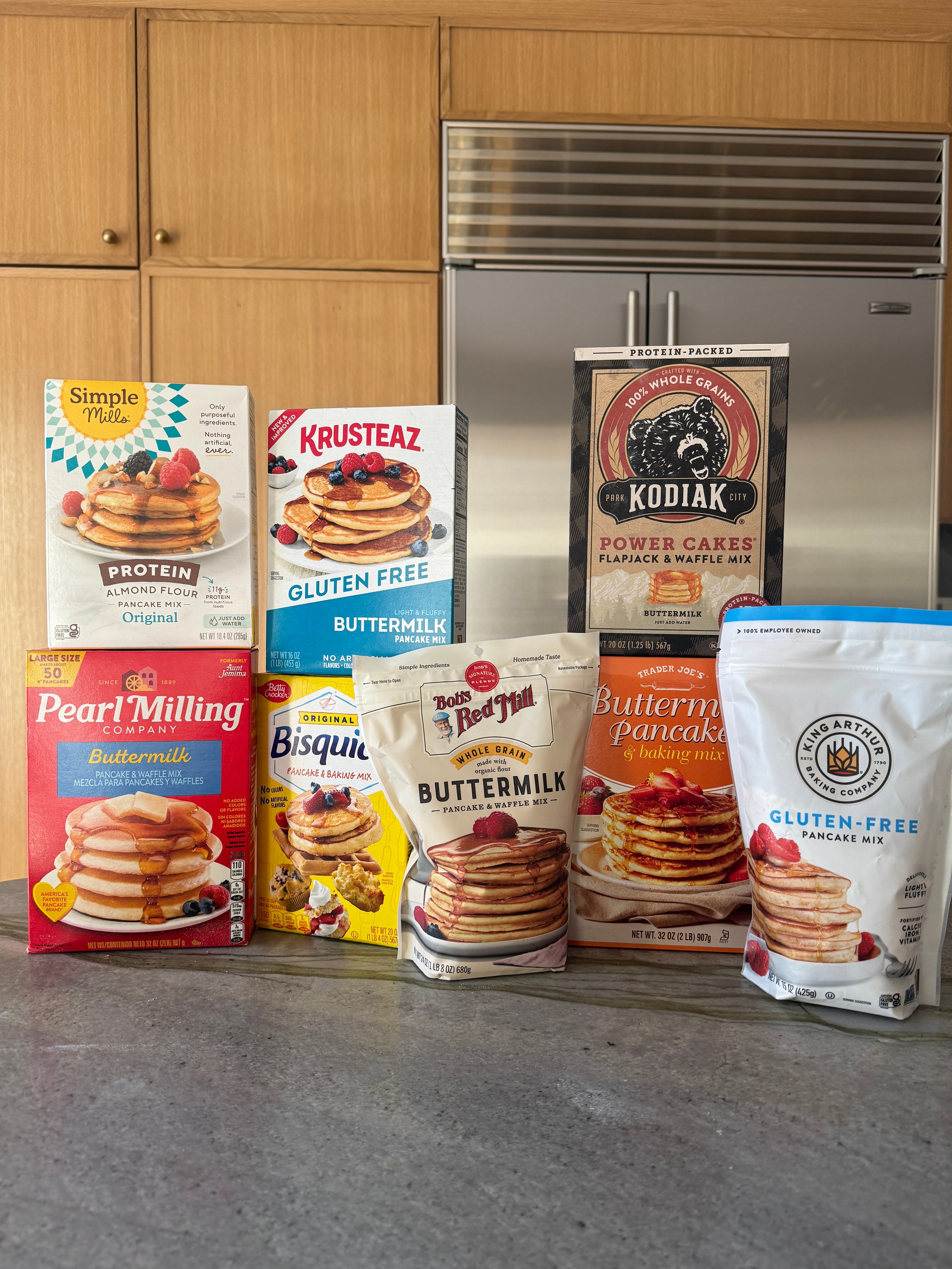 Assortment of various pancake and waffle mix boxes displayed on a countertop, featuring brands like Kodiak, Krusteaz, and Bisquick