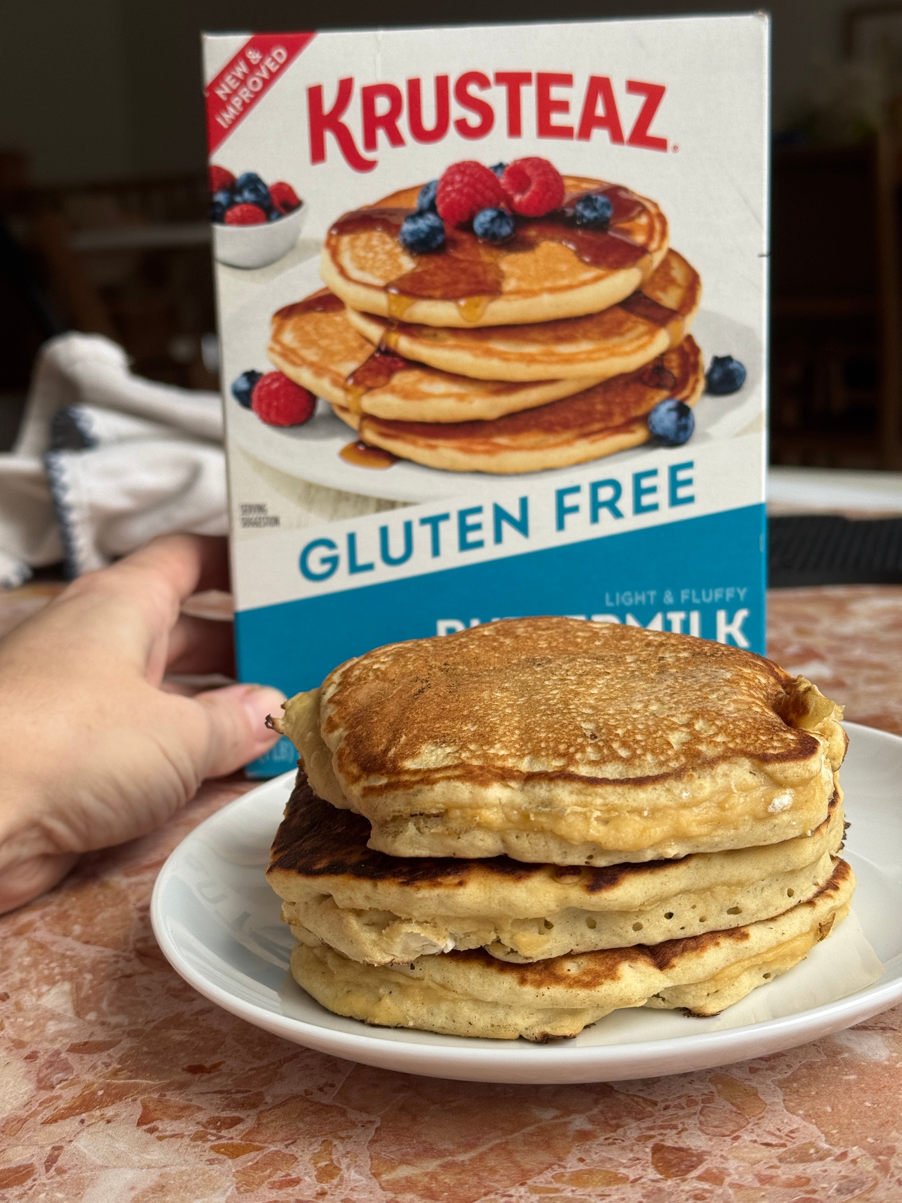 Box of Krusteaz gluten-free pancake mix held behind a plate of freshly made pancakes