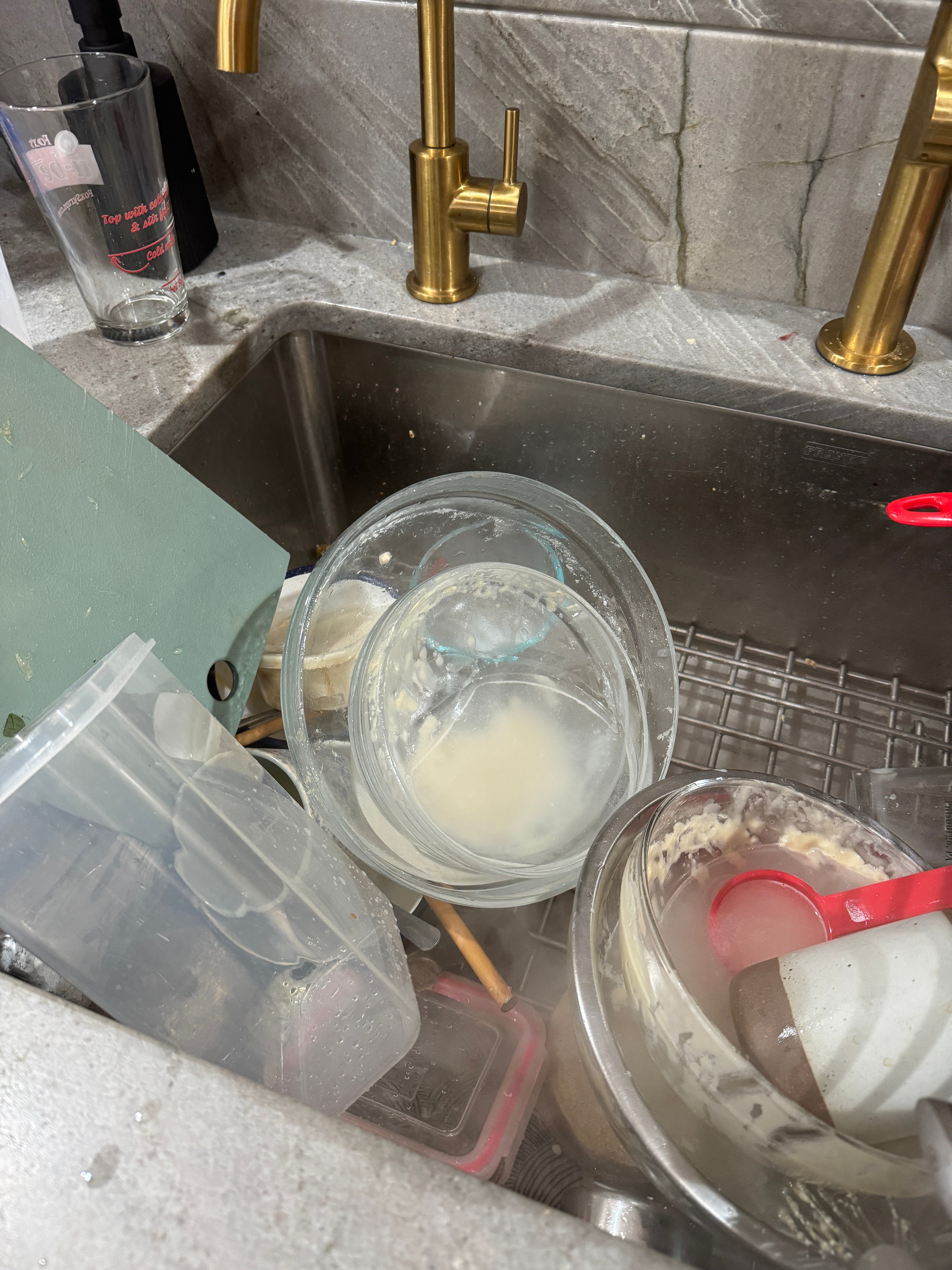 A kitchen sink filled with dirty dishes, containers, and utensils stacked haphazardly