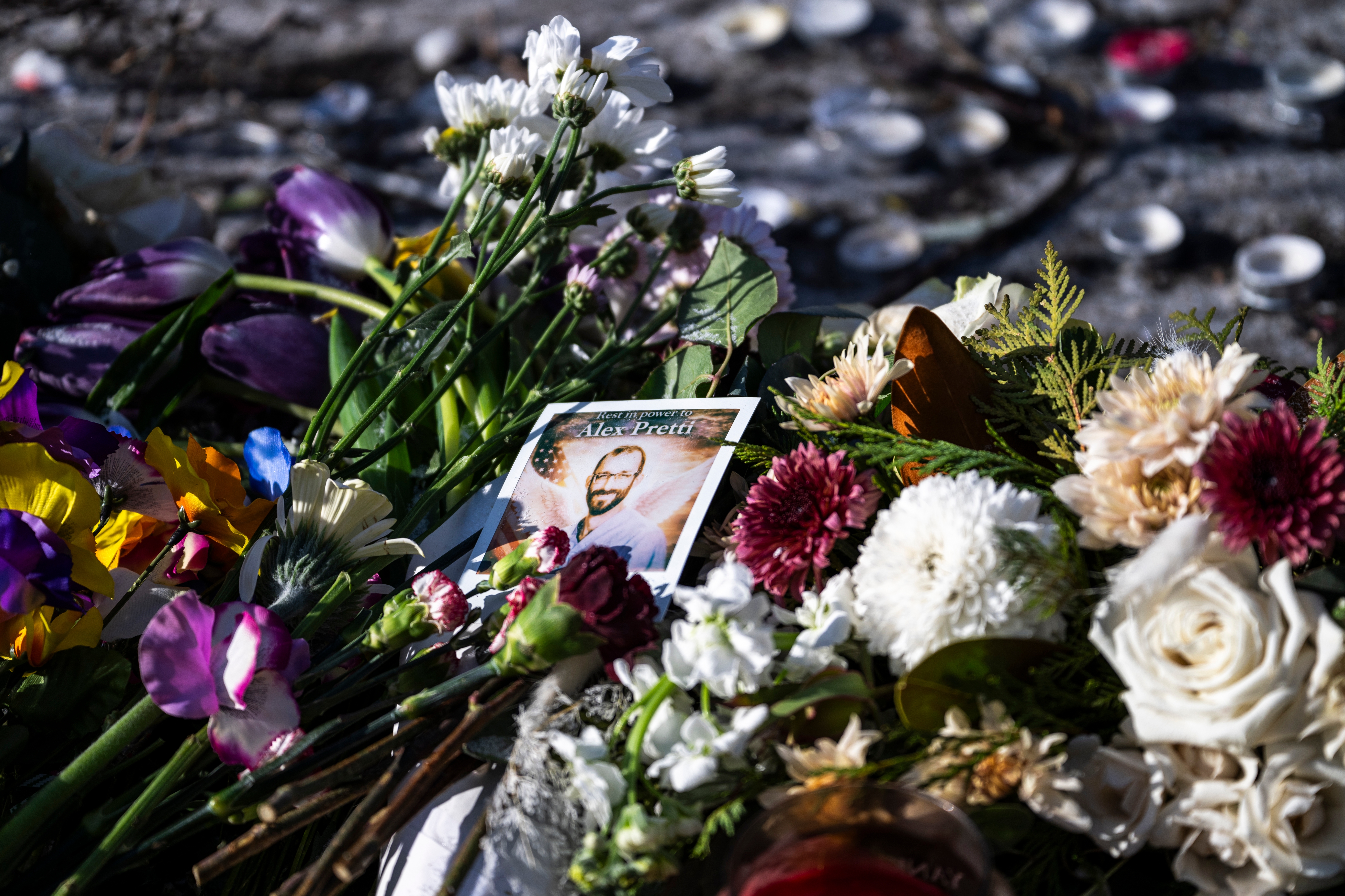 Blomster og et innrammet bilde av en smilende person er plassert på bakken, omgitt av stearinlys til minne om