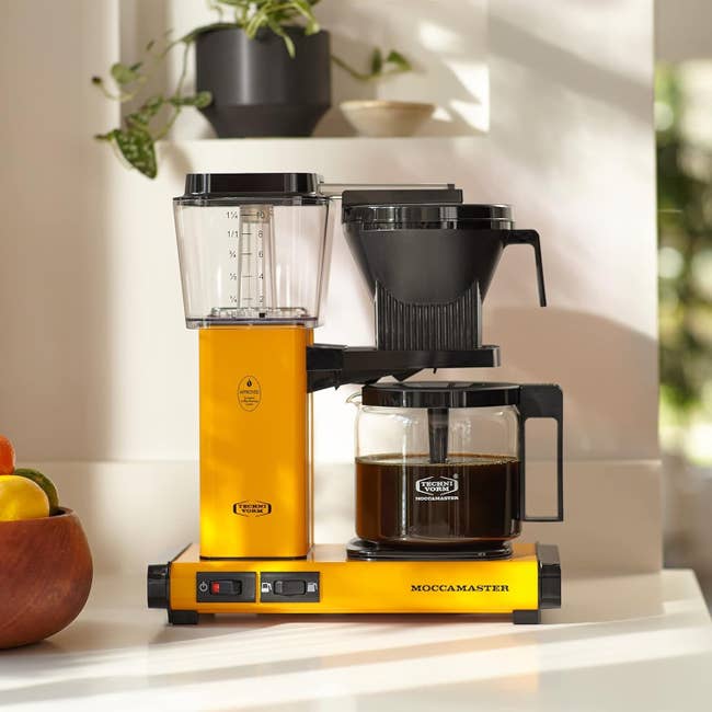 Yellow Moccamaster coffee maker on kitchen counter with plants in the background