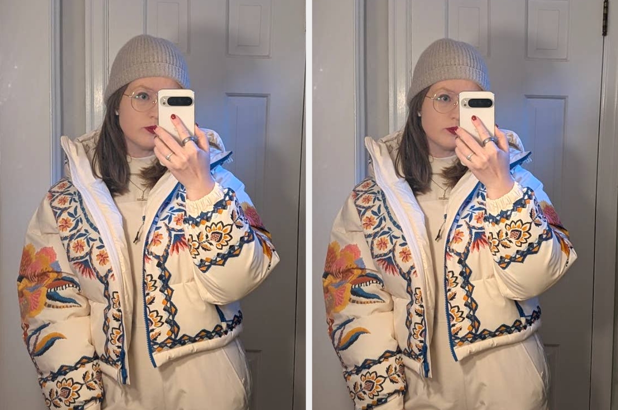 Person wearing a puffer jacket with floral embroidery, holding a smartphone and taking a mirror selfie