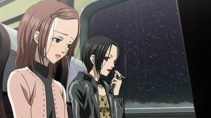 Two animated women sitting by a window on a train, one with long hair and a cardigan, the other with short hair, a leather jacket, and holding a cigarette