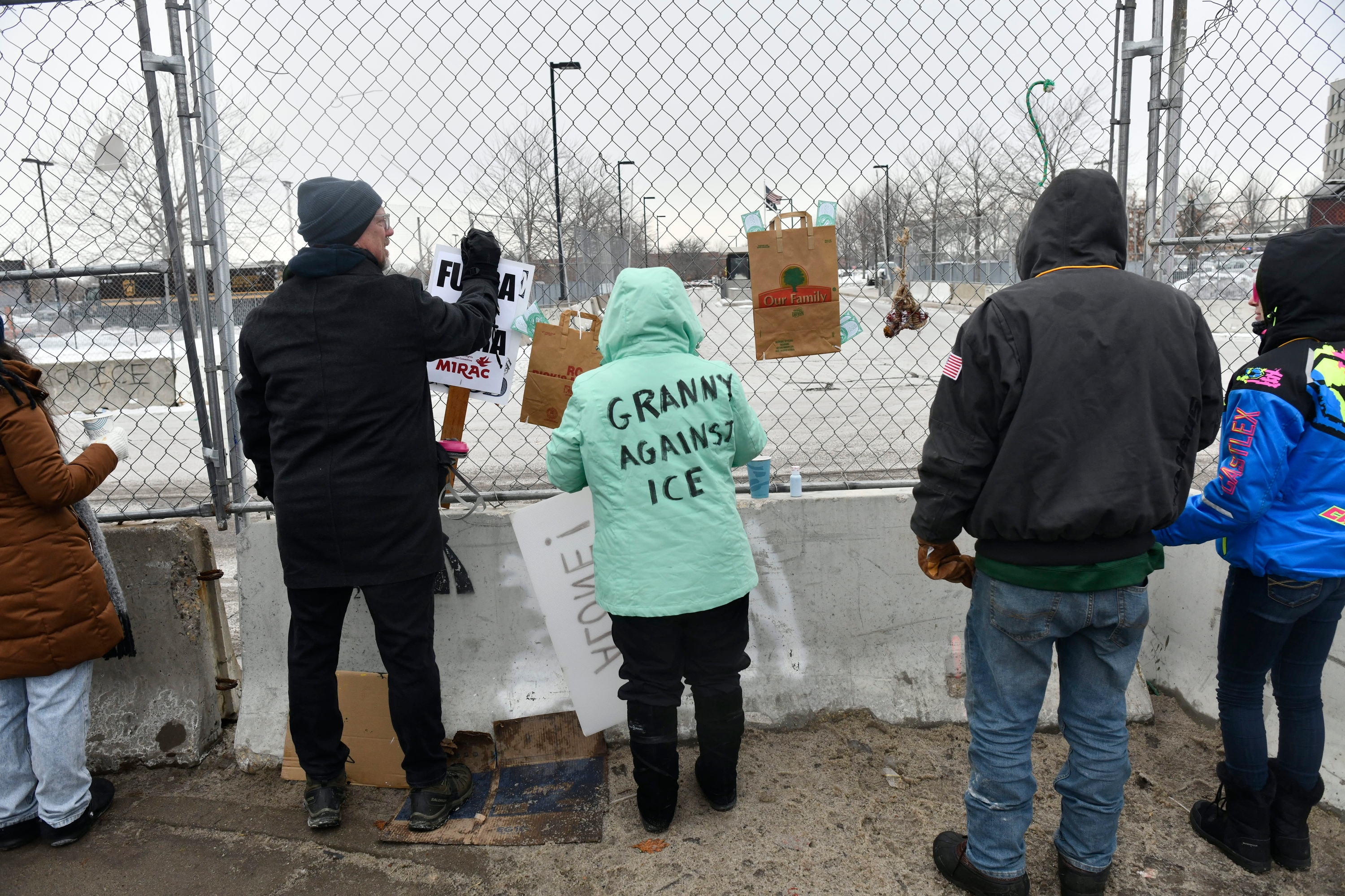 Folk plasserer protestskilt på et gjerde med kjetting. På jakken til én person står det 