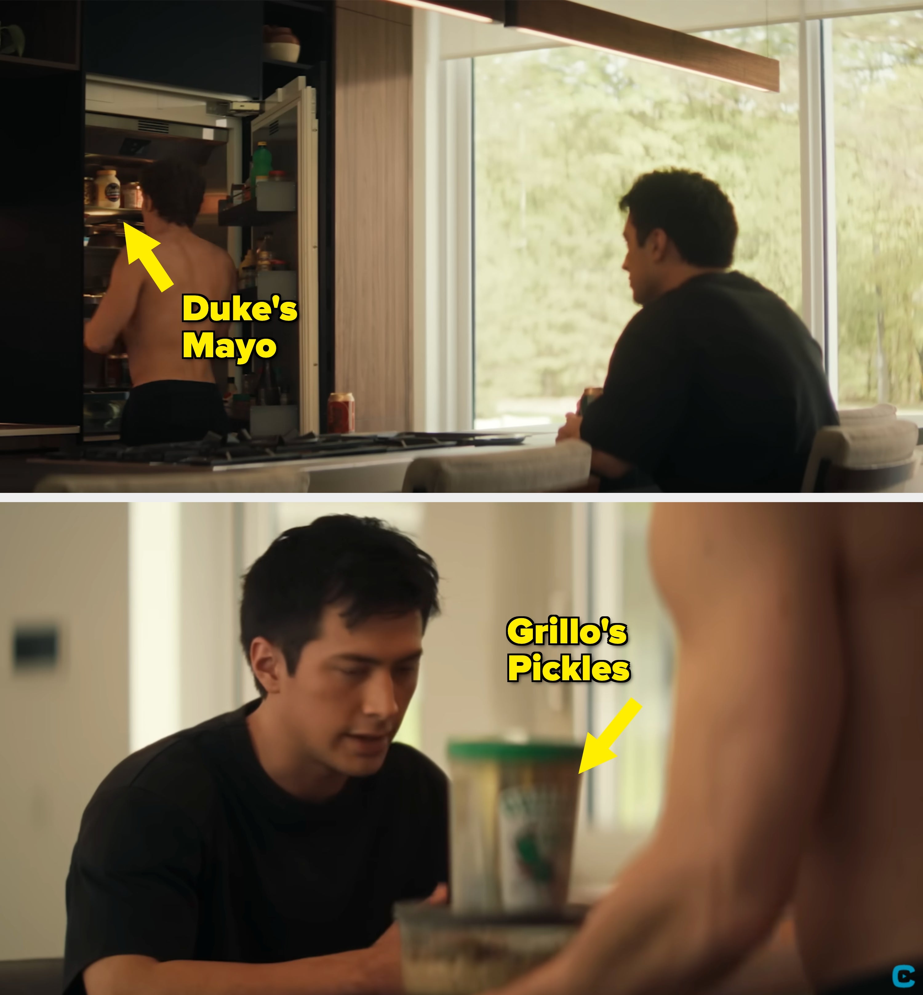 A shirtless person stands in front of an open refrigerator, while another person sits at a kitchen counter looking at them. Large window in background