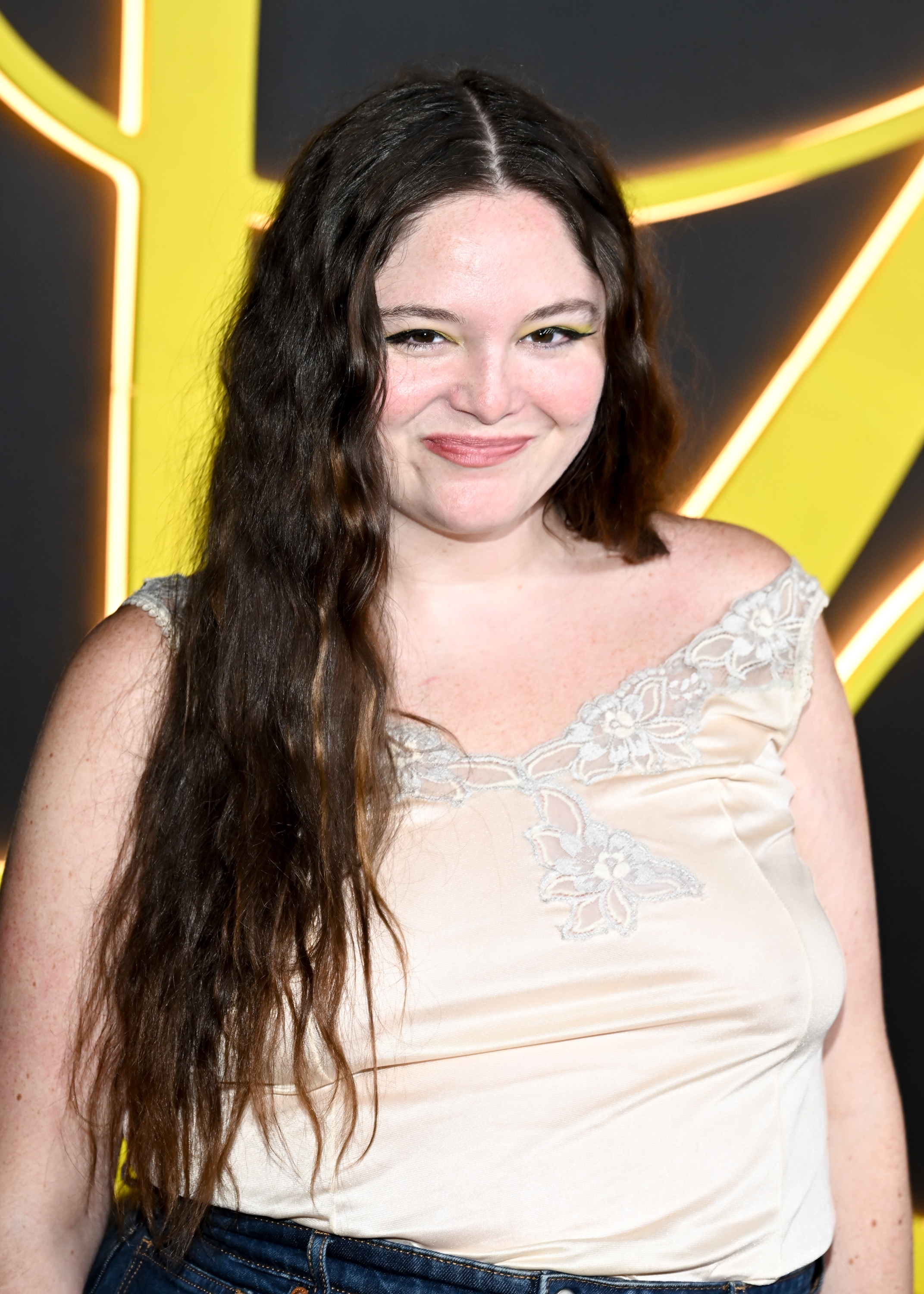 Person med langt hår smiler, iført en blondetrimmet topp, på et formelt arrangement