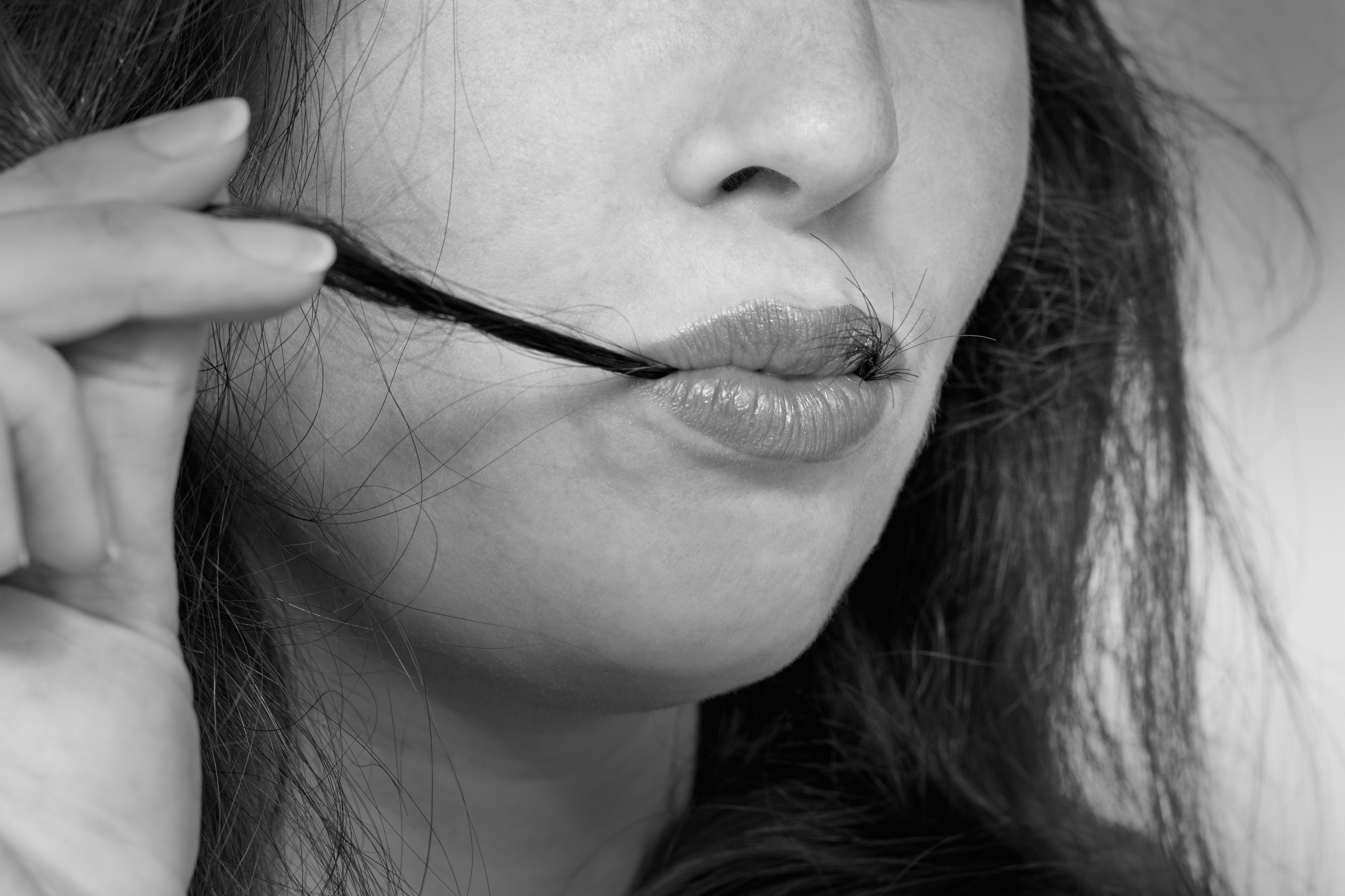 Personen holder forsiktig en hårstrå til leppene sine, fortapt i tanker. Uttrykket deres antyder kontemplasjon eller dagdrømmer