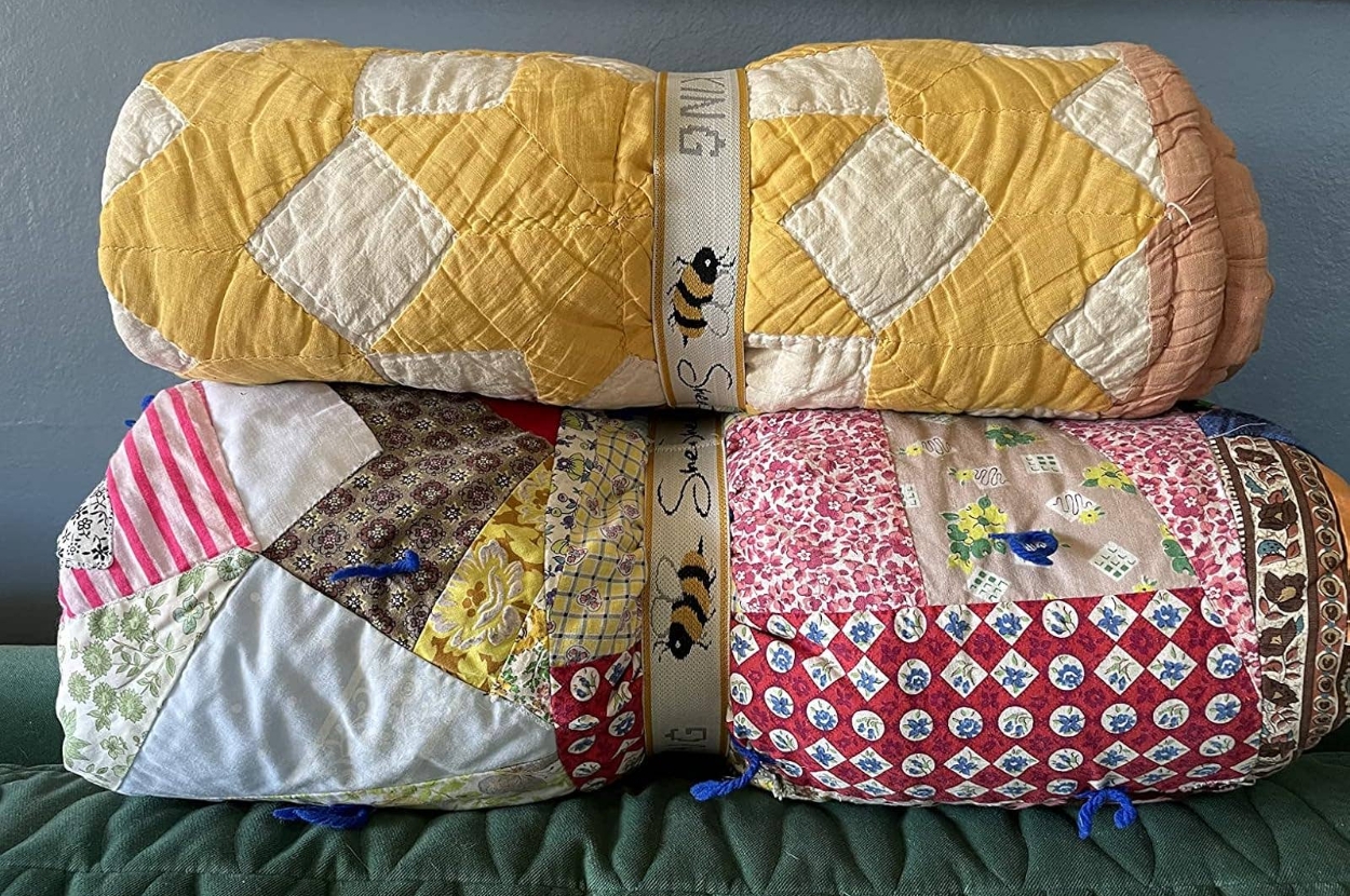 Two rolled, patterned quilts with diamond and patchwork designs, suitable for adding cozy texture to a room