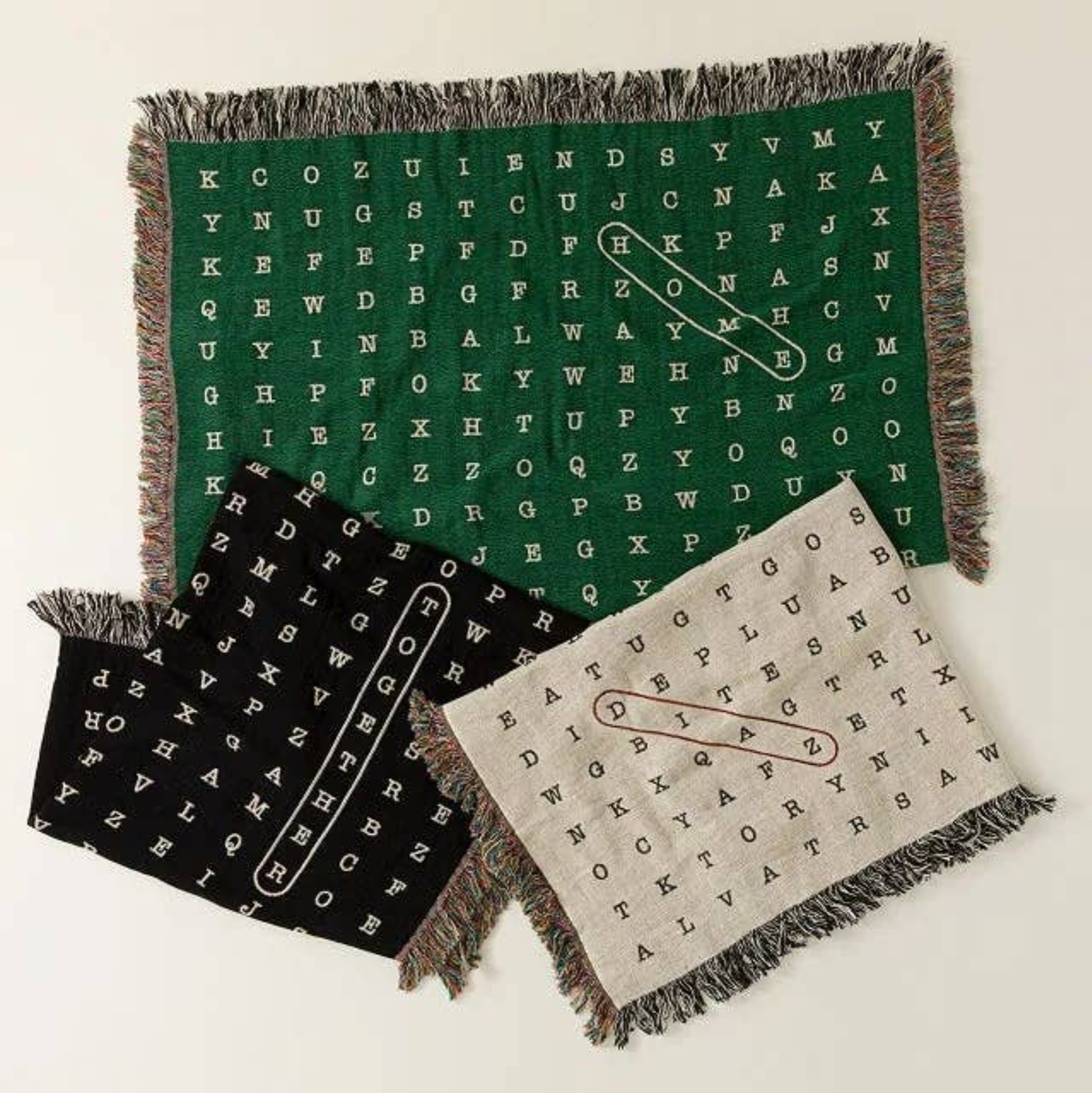 Three woven blankets featuring word search-style patterns and fringe edges, designed as stylish home decor items