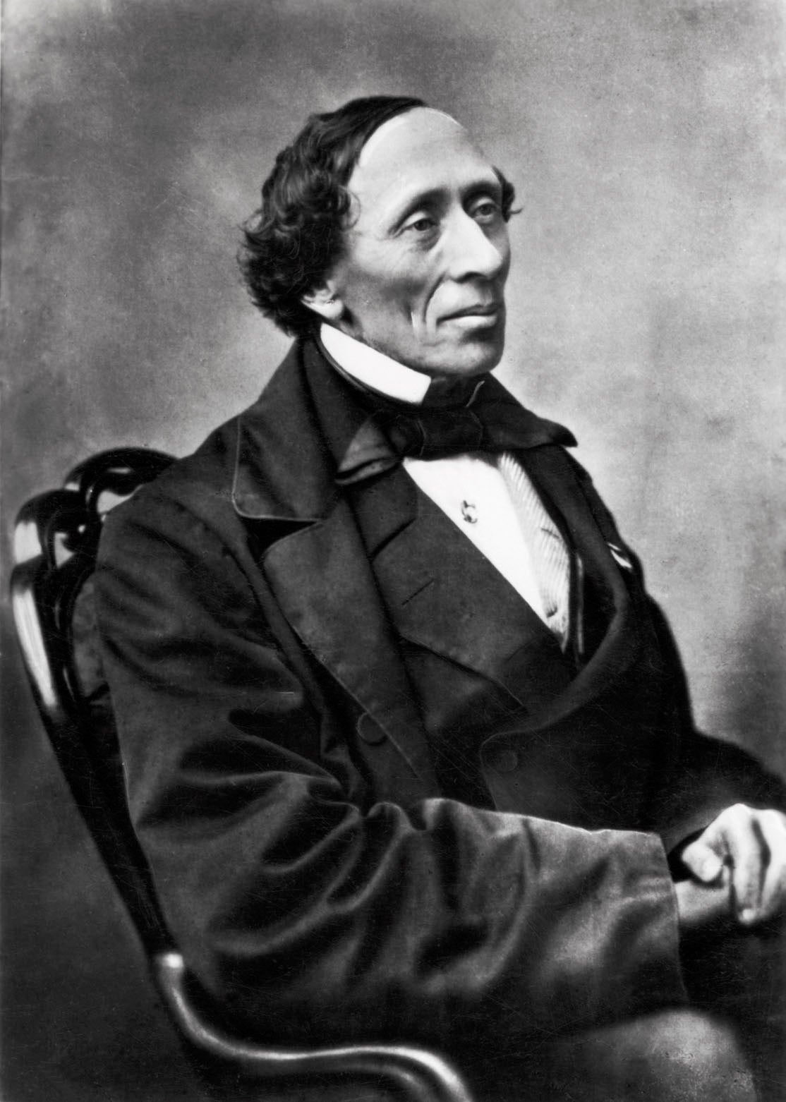 A historical black-and-white portrait of a man wearing a formal suit with a bow tie, sitting in a chair