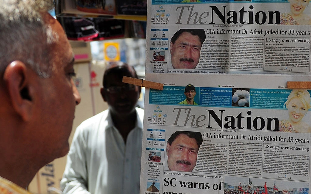 Mann leser en avisoverskrift om CIA-informant Dr. Afridi som er fengslet i 33 år, vist i et stativ