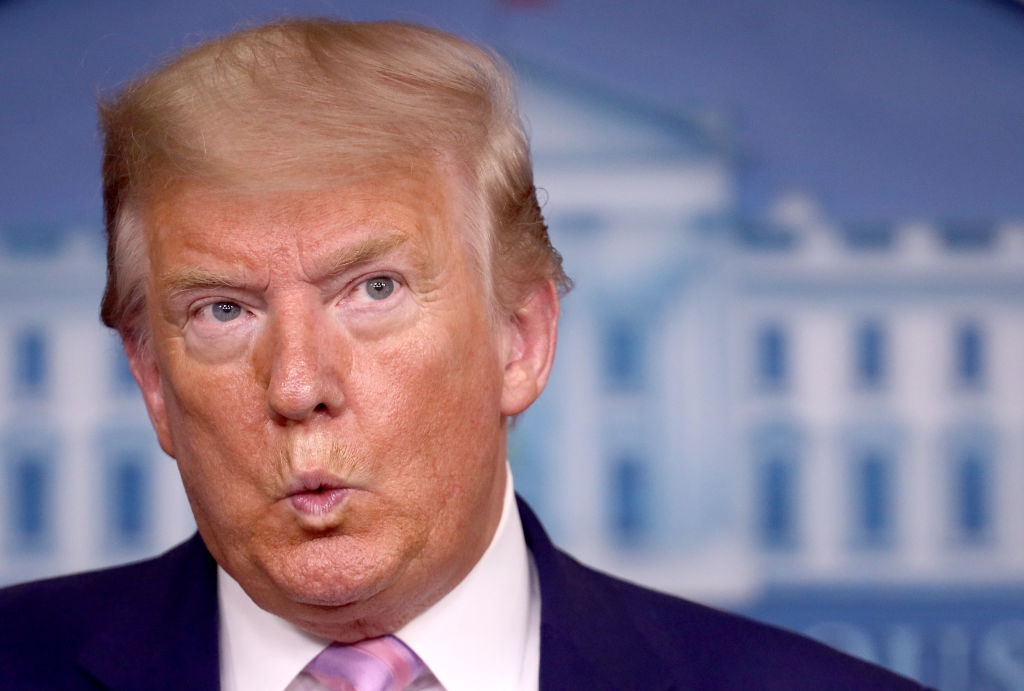 En person lager et overrasket ansiktsuttrykk med sammenknepte lepper, og står foran en uskarp bakgrunn som ligner en regjeringsbygning