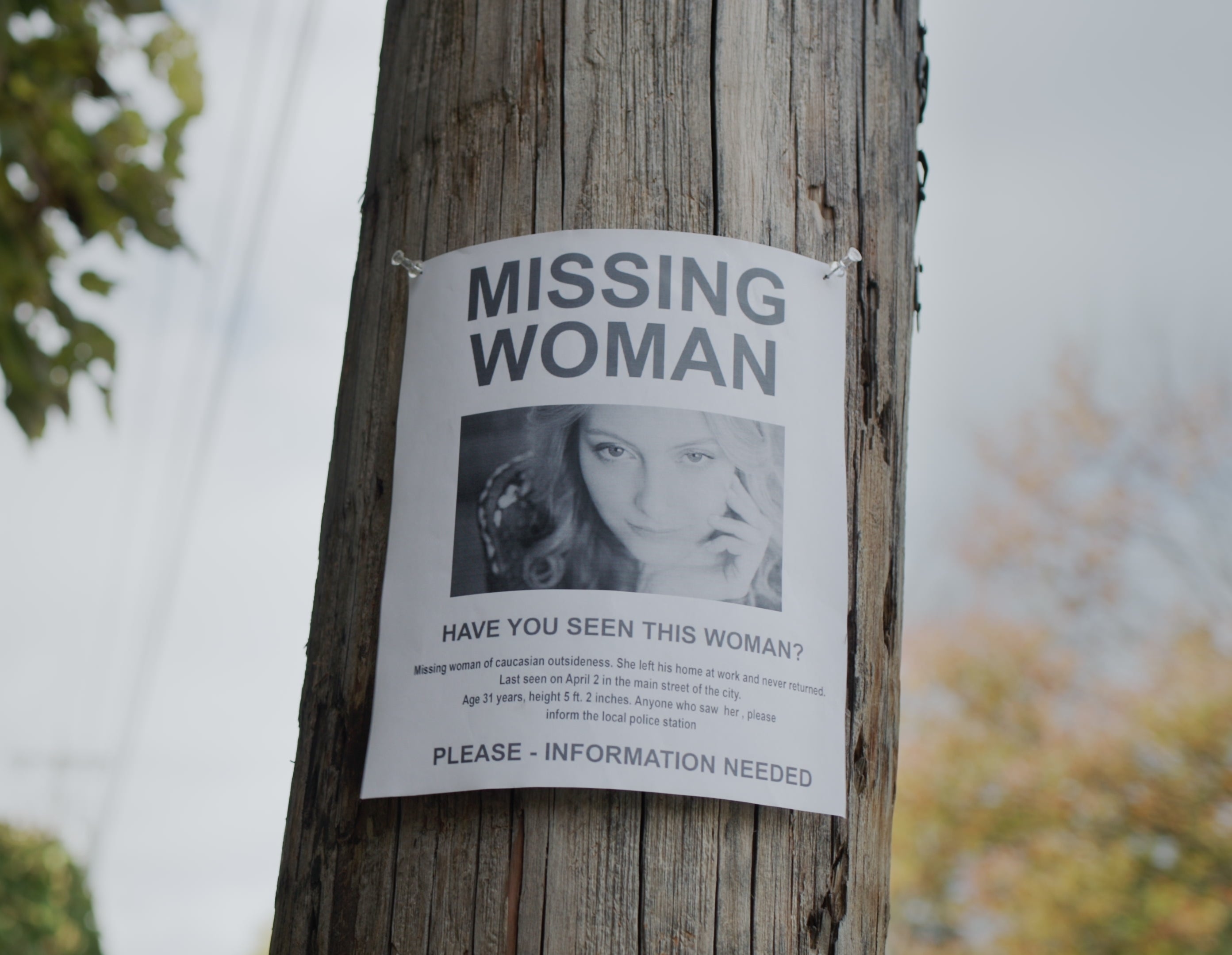 Savnet person-plakat for en kvinne festet på en trestang. Plakaten ber om informasjon og inkluderer et bilde av kvinnen