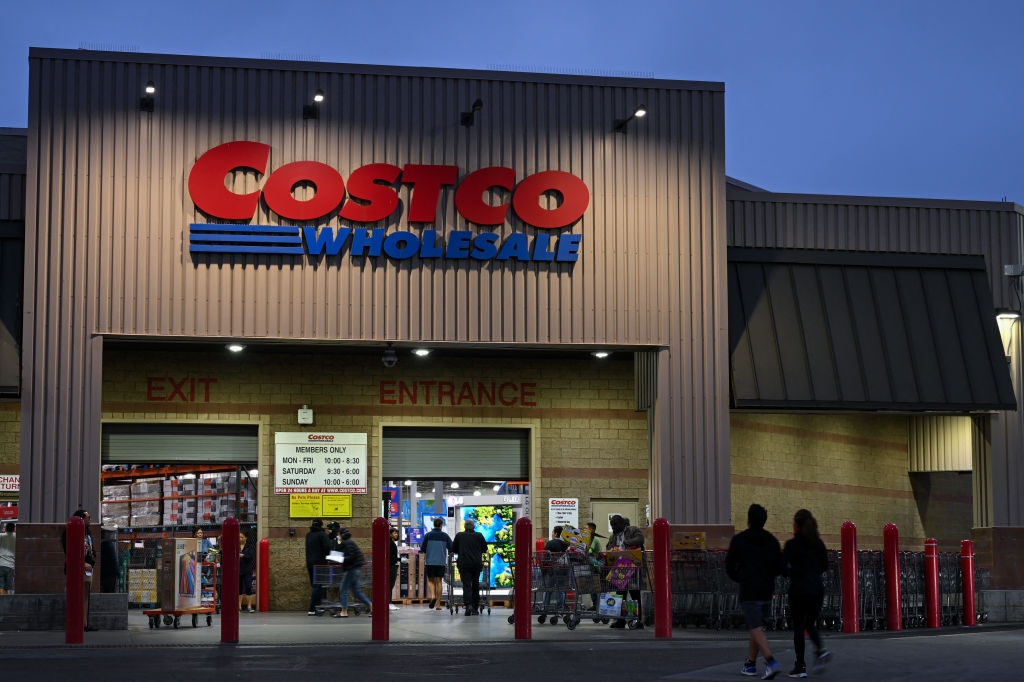Folk som går inn og ut av en godt opplyst Costco Wholesale-butikk om kvelden. Butikkens navn vises tydelig over inngangen