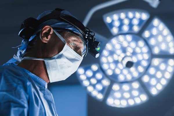 Surgeon wearing surgical gear and headlight, focused on a procedure in an operating room, with bright surgical lights in the background
