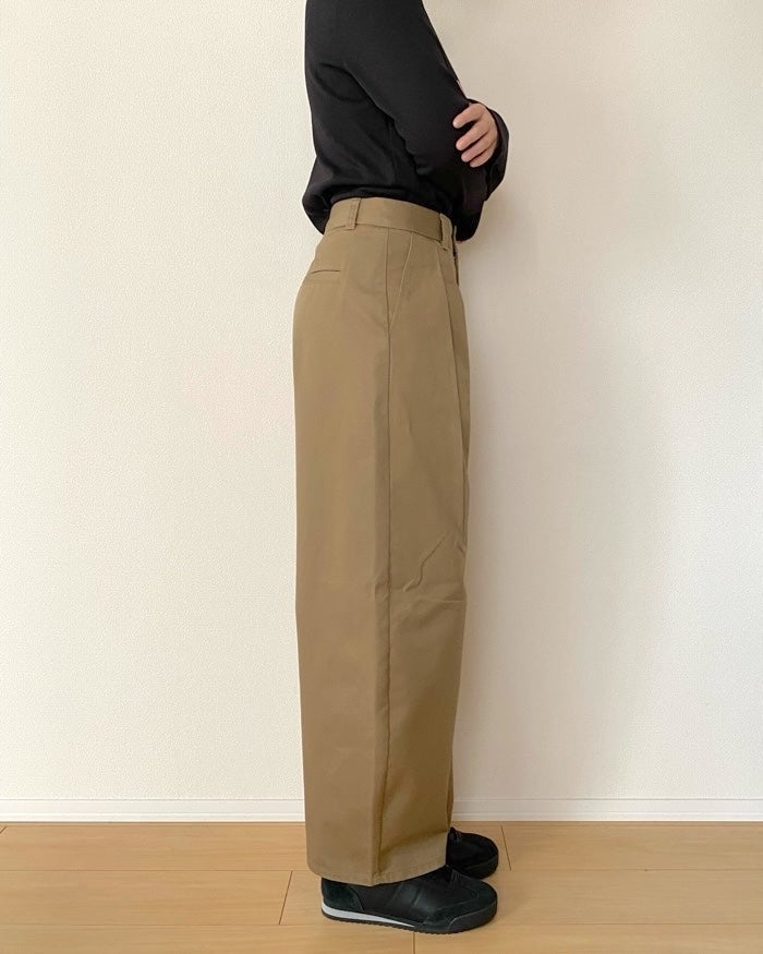 GU（ジーユー）の「チノタックバレルパンツQ」黒いシャツとブラウンのパンツを着た人が横向きに立っている。