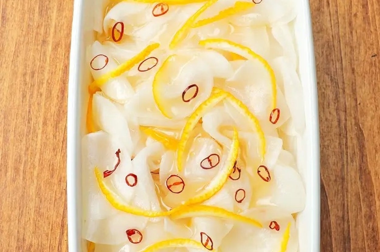 白い皿に盛られた大根と柚子の漬物。薄切りされた大根と黄色い柚子の皮、赤い唐辛子が散りばめられている。