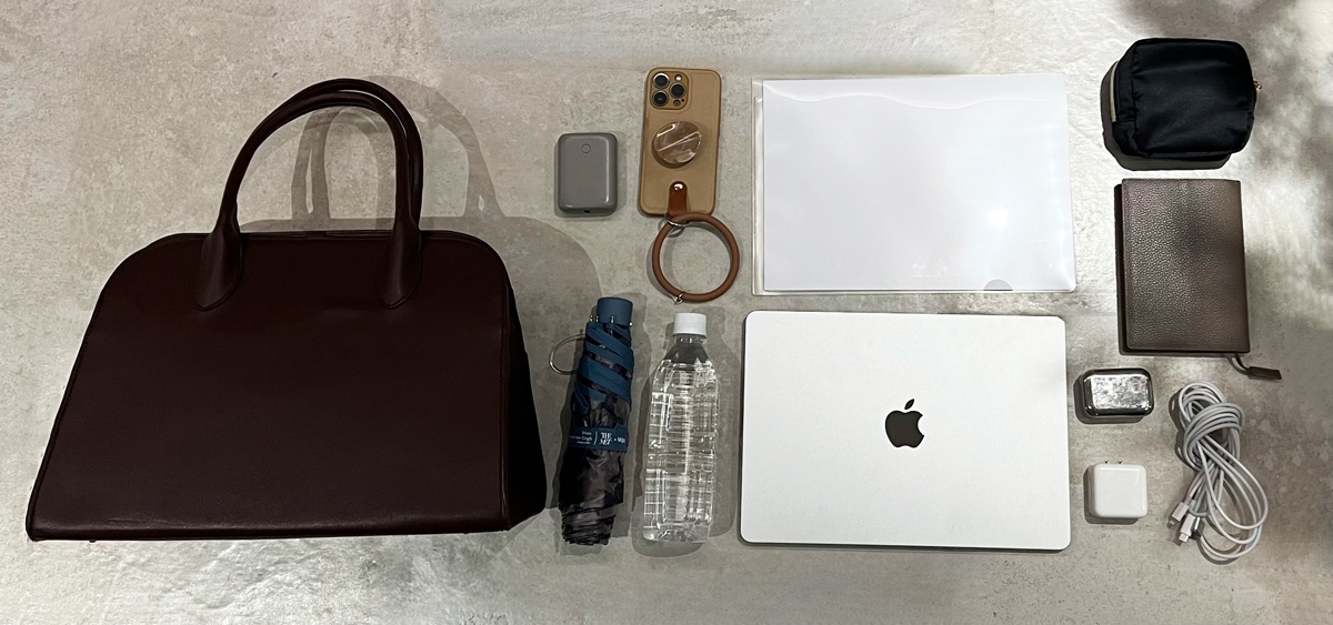A neatly arranged collection of items from a handbag, including a phone, laptop, water bottle, umbrella, wallet, and various tech accessories