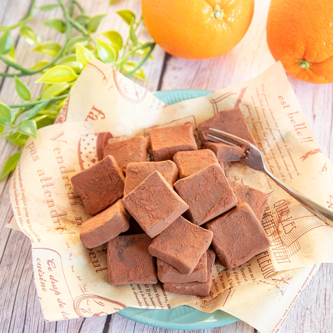 生チョコレートが皿に盛られており、背景にはオレンジと緑の葉が見える。