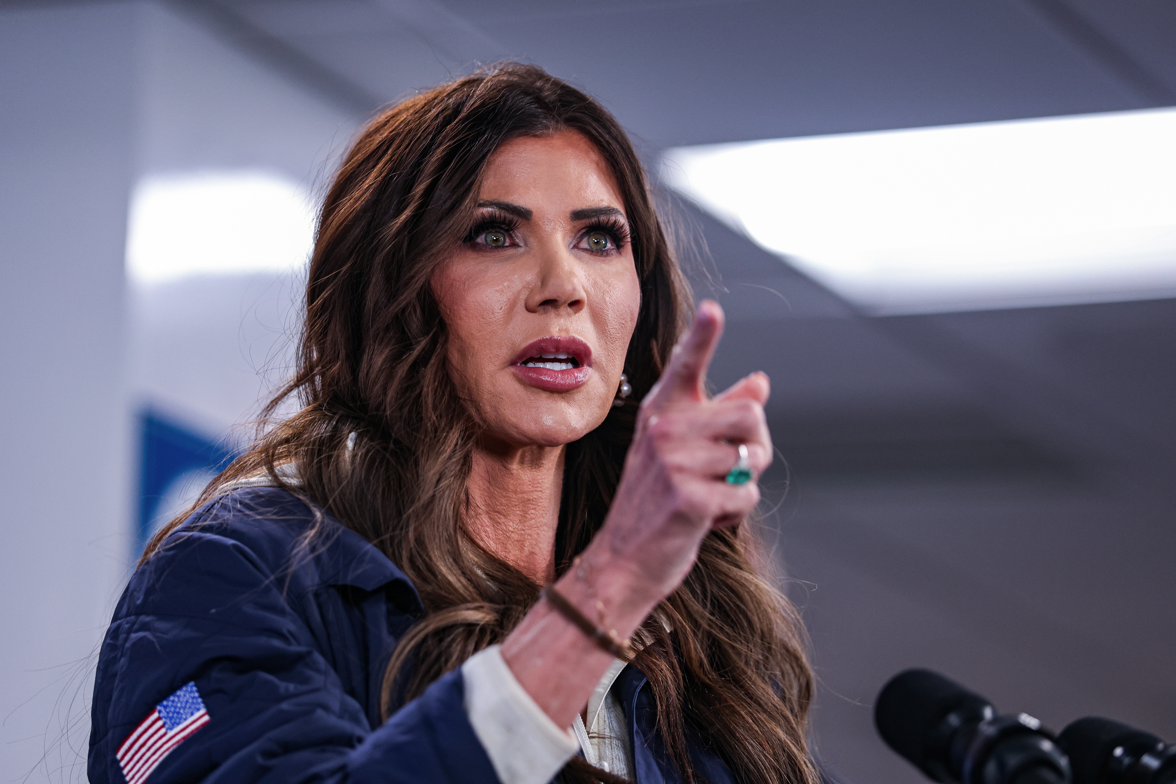 En person snakker lidenskapelig ved et podium, gestikulerer med hånden, kledd i formell antrekk som passer for en pressekonferanse.