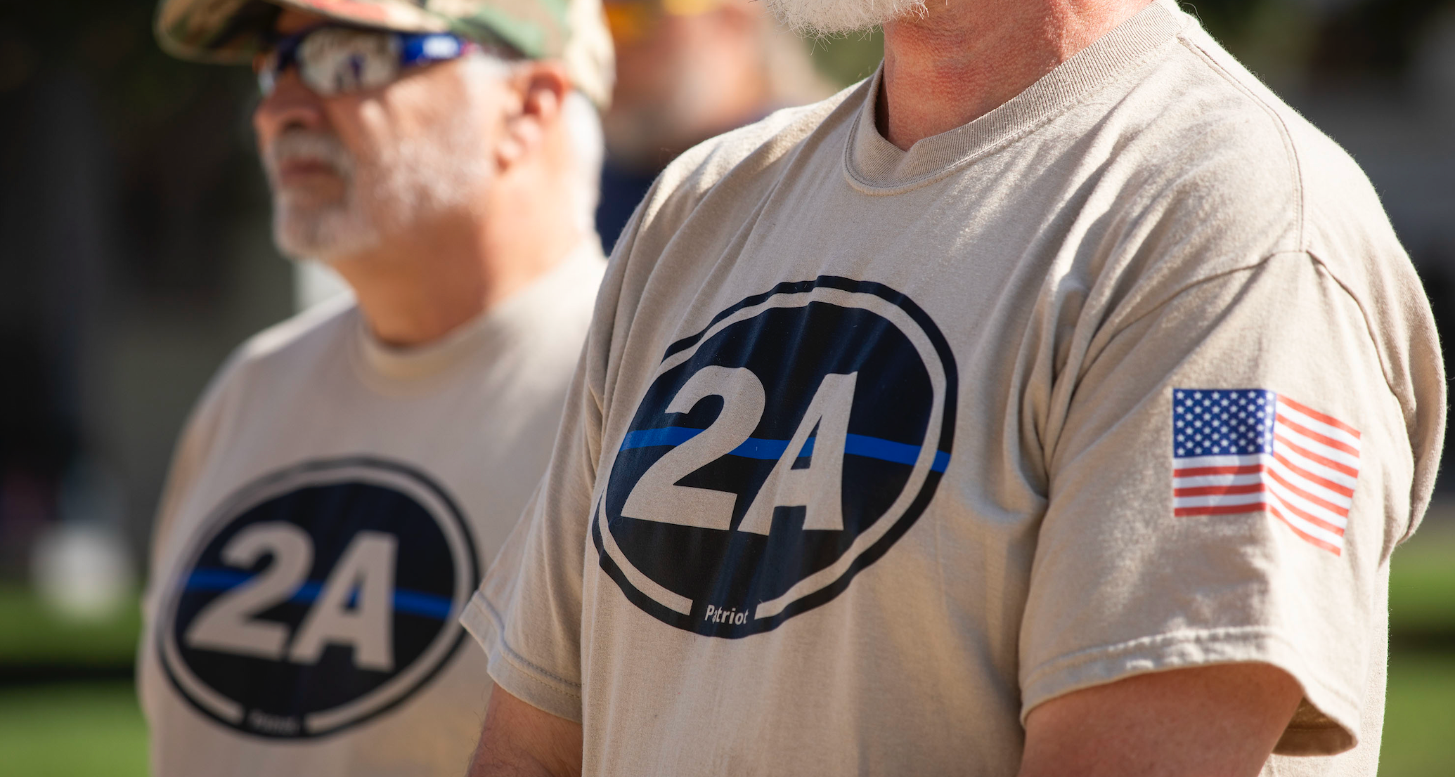 To menn har på seg matchende "2A" skjorter med amerikansk flagglapp på en offentlig sammenkomst