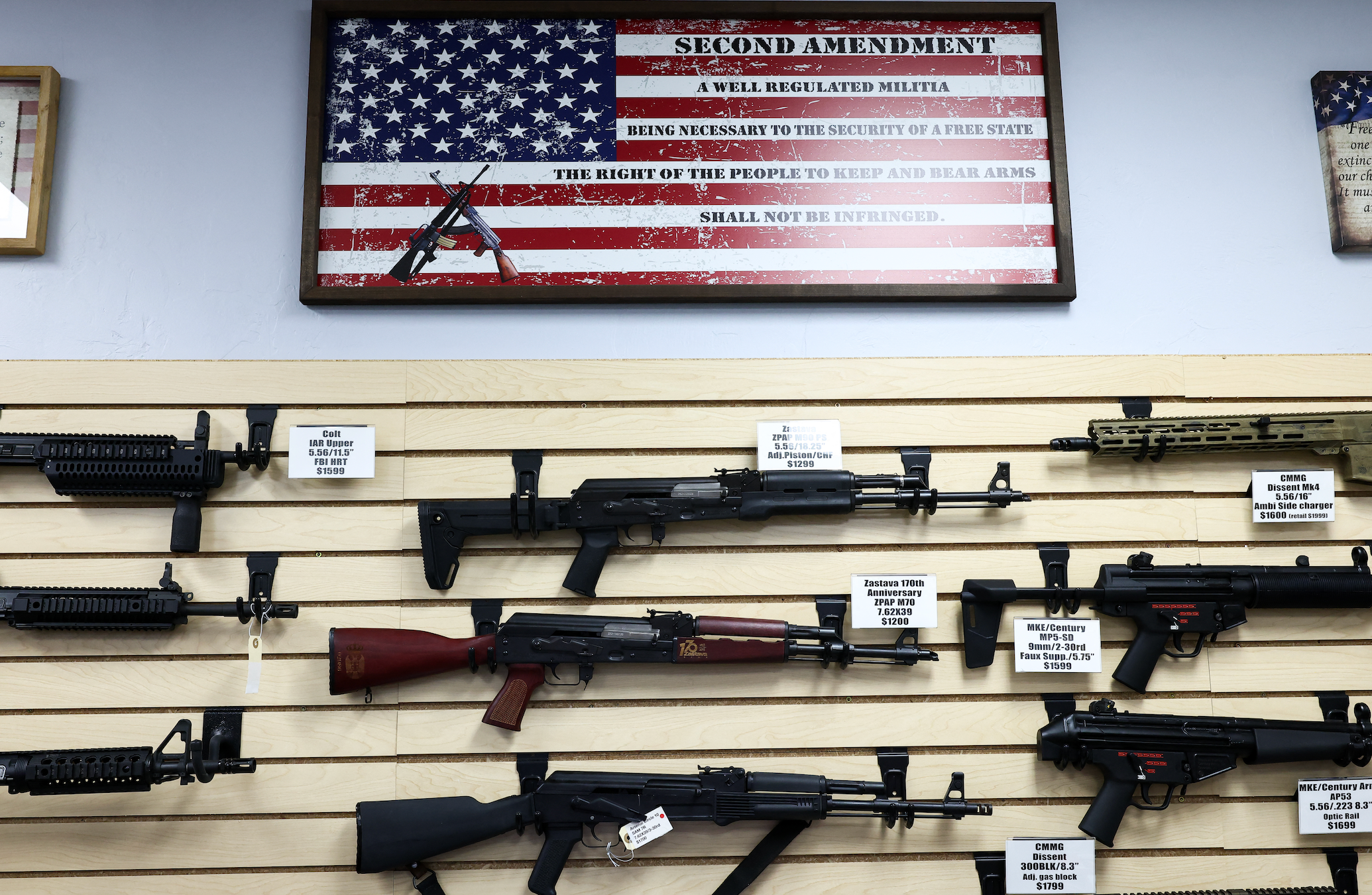 Veggutstilling av rifler i en våpenbutikk, med en innrammet plakett over som siterer den andre endringen av den amerikanske grunnloven