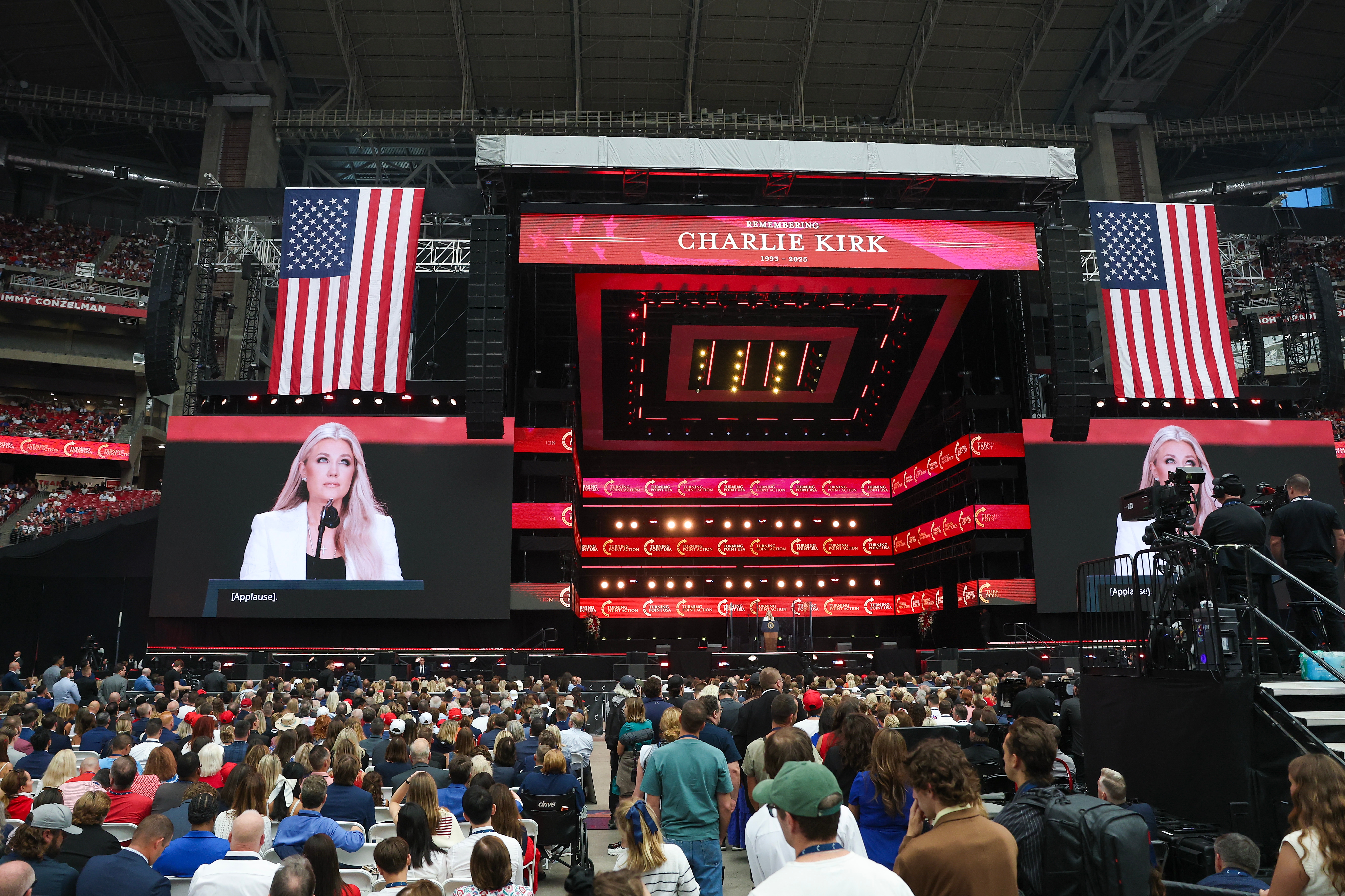 Stort innendørs arrangement med en høyttaler på scenen, sittende publikum og
