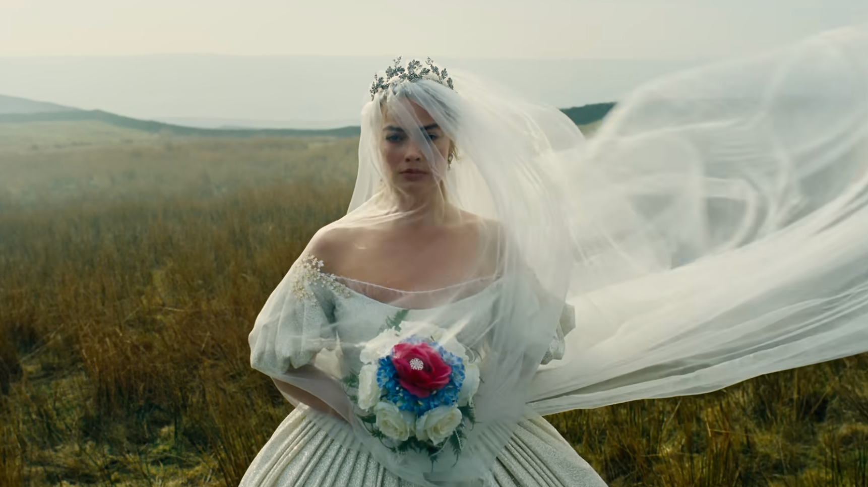 A person outdoors in a wedding dress with a long veil and floral headpiece, holding a bouquet of flowers