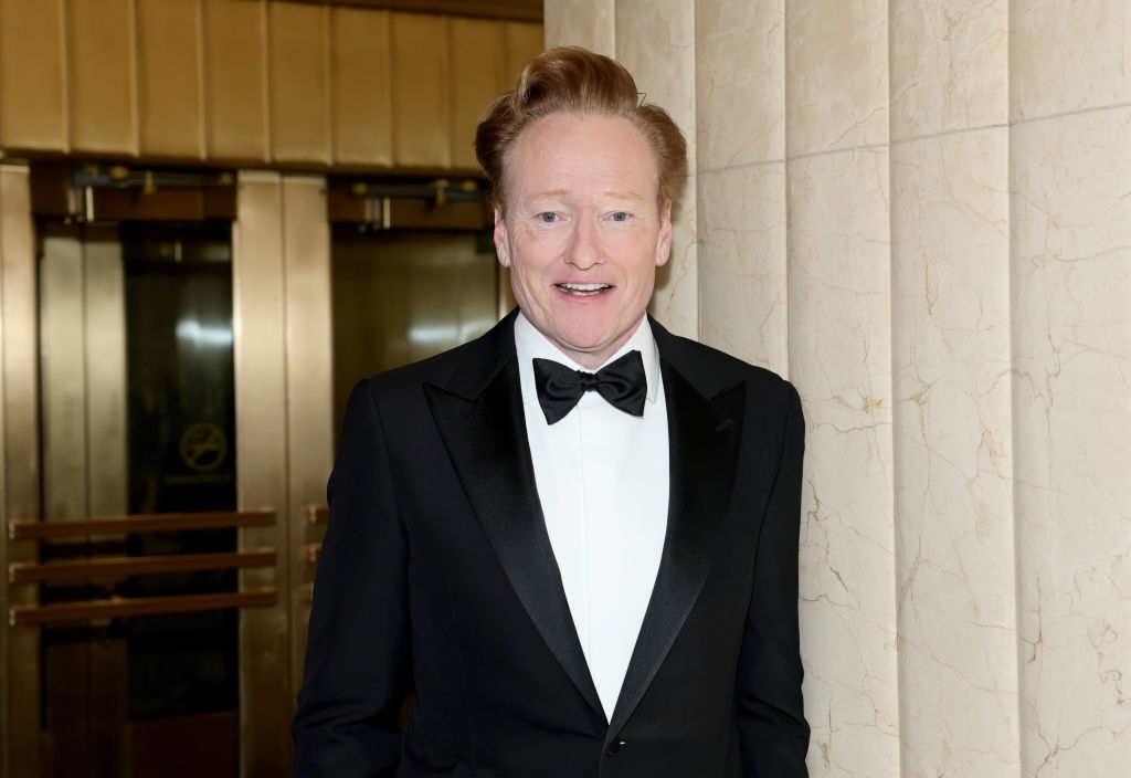 Person in a formal black tuxedo and bow tie, smiling in an indoor setting