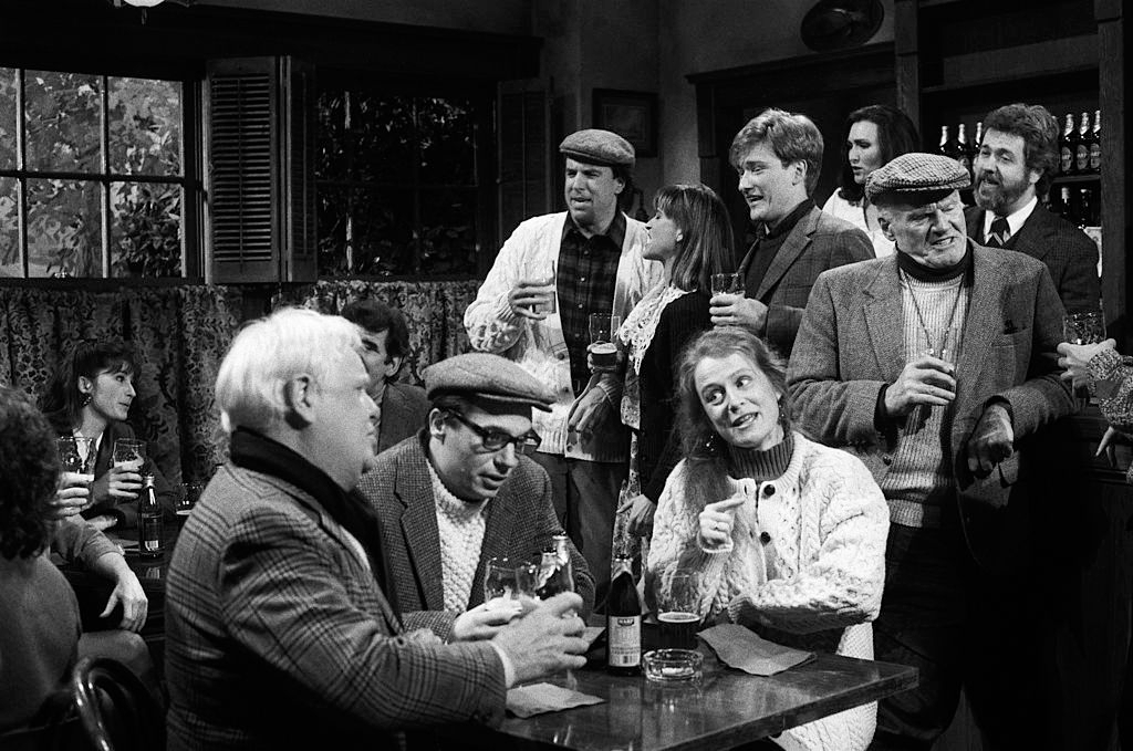 A lively pub scene with people in vintage clothing and flat caps, engaged in conversation and holding drinks