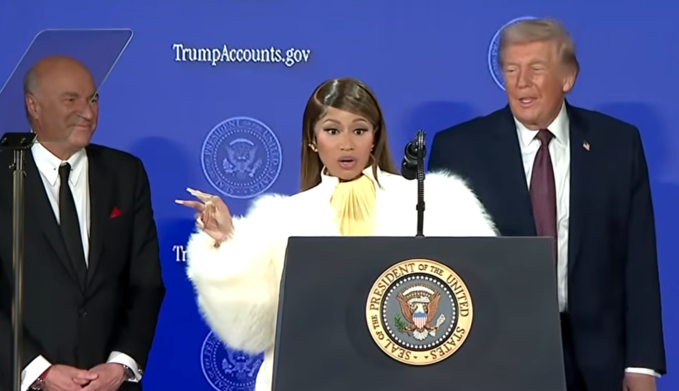 Jeg vet ikke hvem disse menneskene er. En person i et mykt hvitt antrekk står ved et podium og snakker, med to personer i dress på hver side