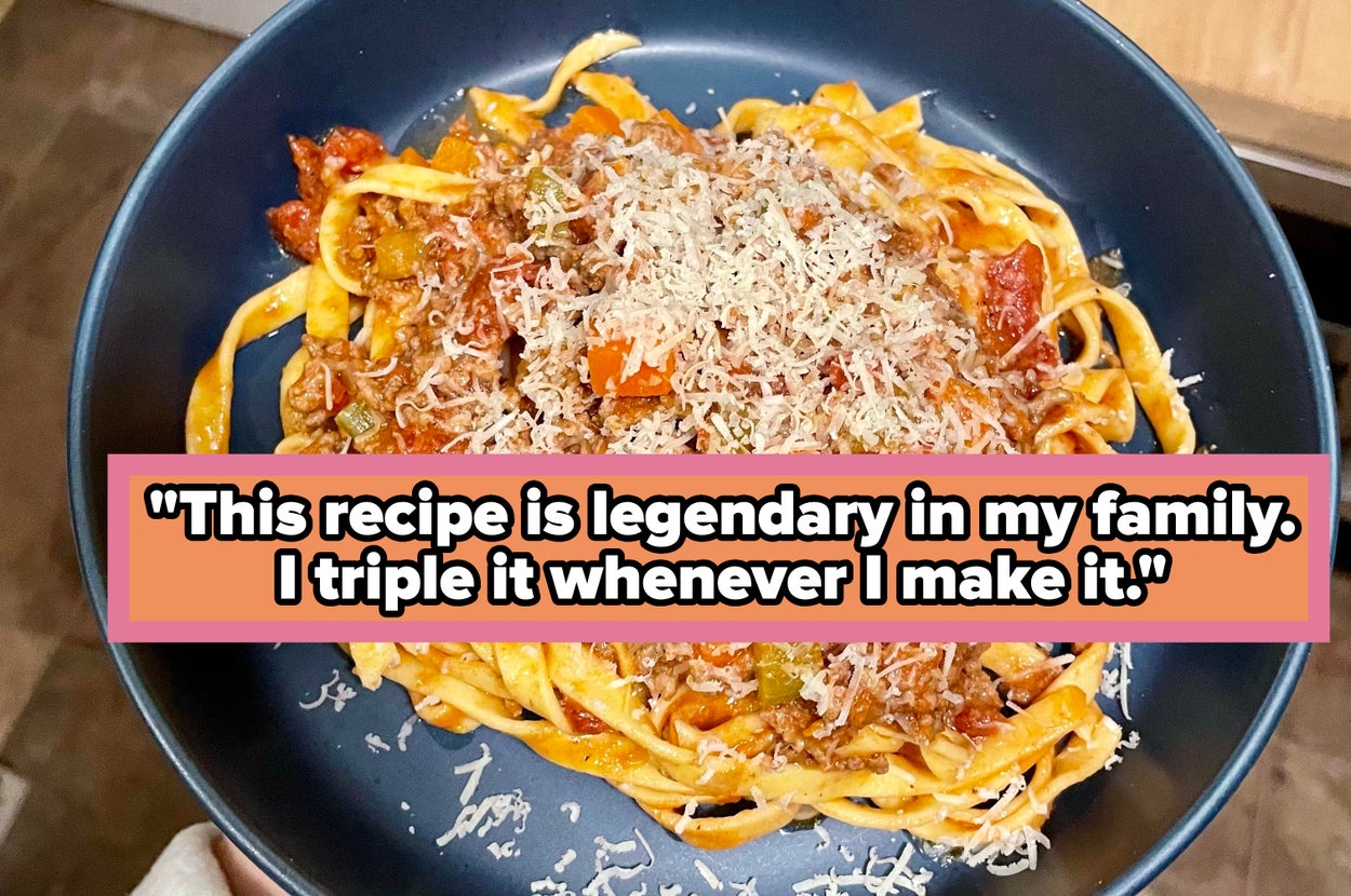 A plate of pasta topped with meat sauce and grated cheese, held over a tiled kitchen floor
