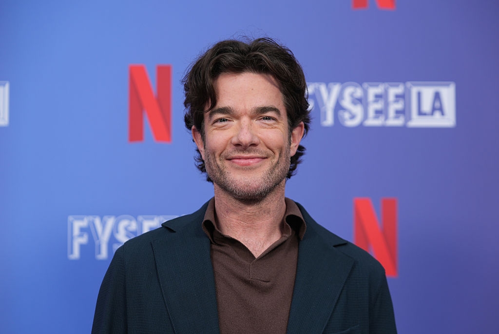 Person smiling at a Netflix event, wearing a dark blazer over a brown shirt, standing against a branded background