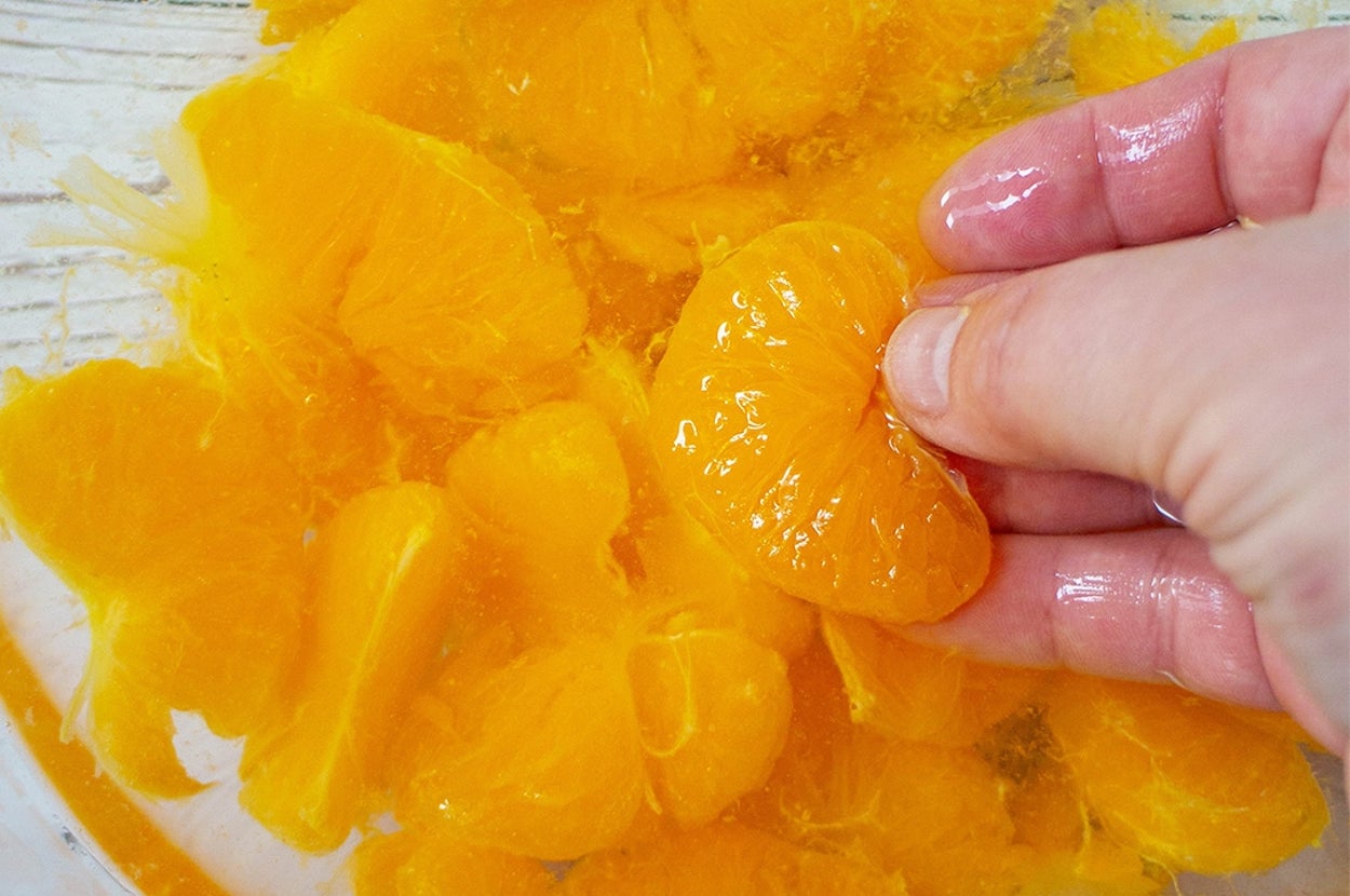 手に持ったみかんの房が他のみかんの房の上に重なっている様子。