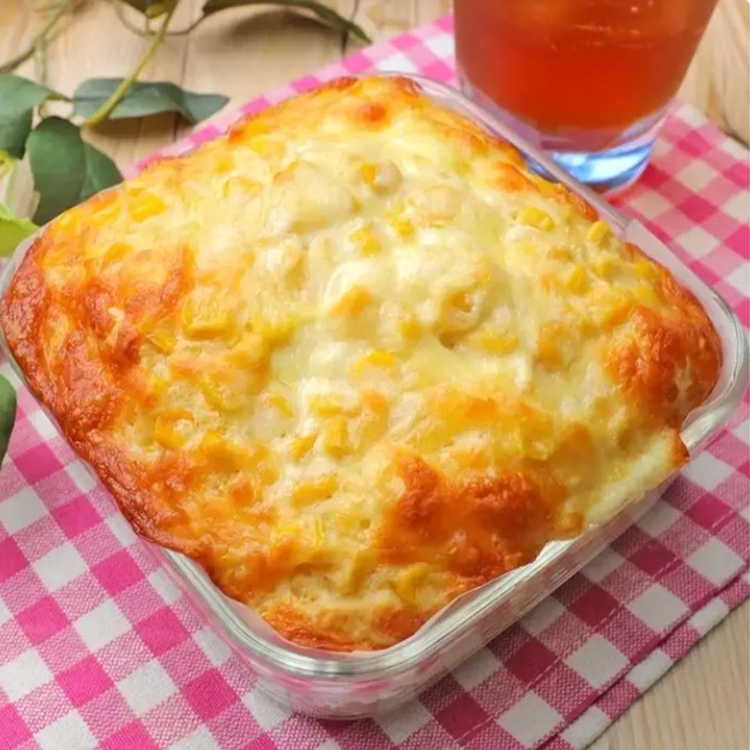 ガラス容器に焼き上がったグラタンがあり、隣には冷たい飲み物が置かれています。背景にピンクのチェック柄のクロス。