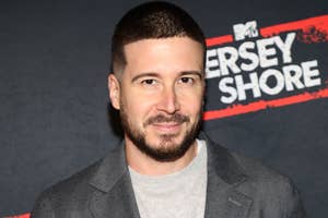 Vinny Guadagnino poses on a red carpet wearing a casual suit jacket over a light shirt with an MTV Jersey Shore backdrop