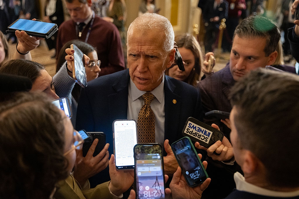 En mann i dress er omgitt av journalister som holder mikrofoner og smarttelefoner, og fanger hvert ord han sier i overfylte omgivelser