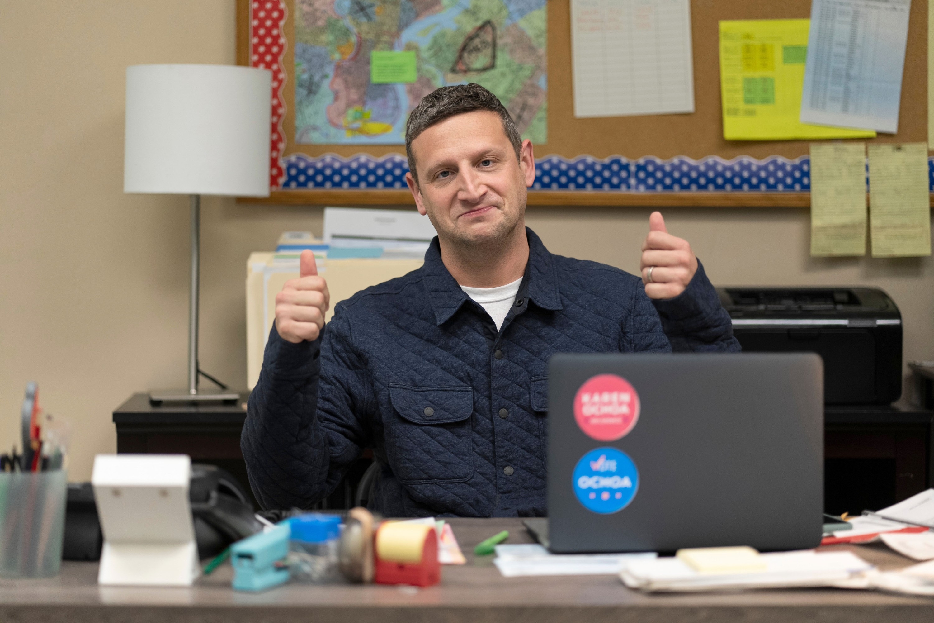 Person seated at an office desk, smiling, and giving two thumbs up