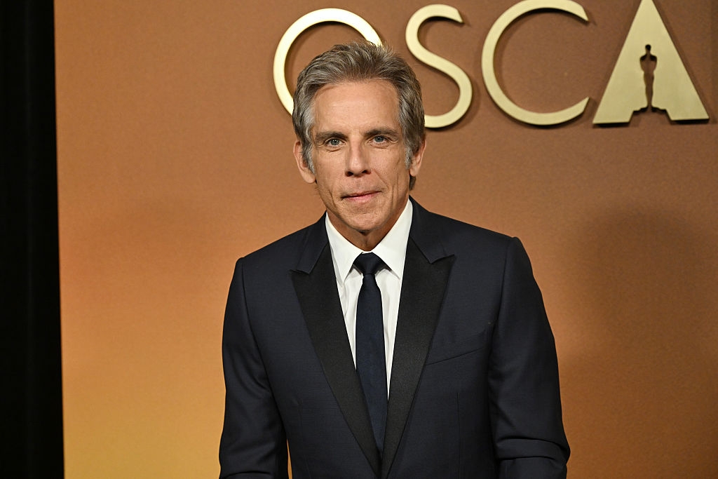 Person in a suit poses at an Oscars event backdrop
