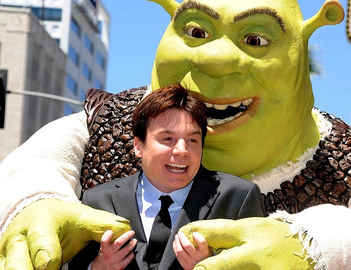 Person in a suit playfully posing with a life-sized costume character of Shrek at an event