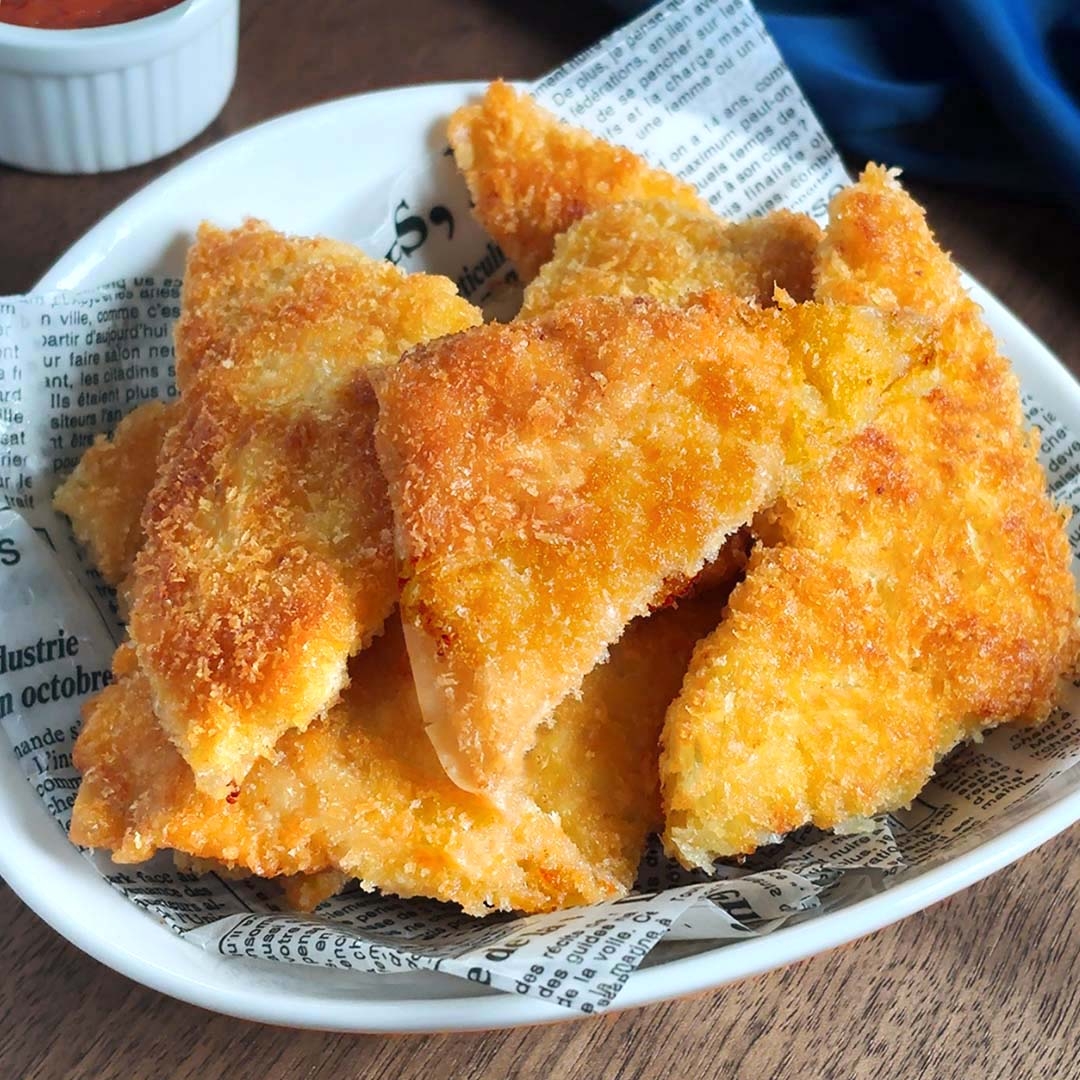 皿に盛られたカツのピースが新聞紙風の紙に載っている。背景にディップ用のソースが見える。