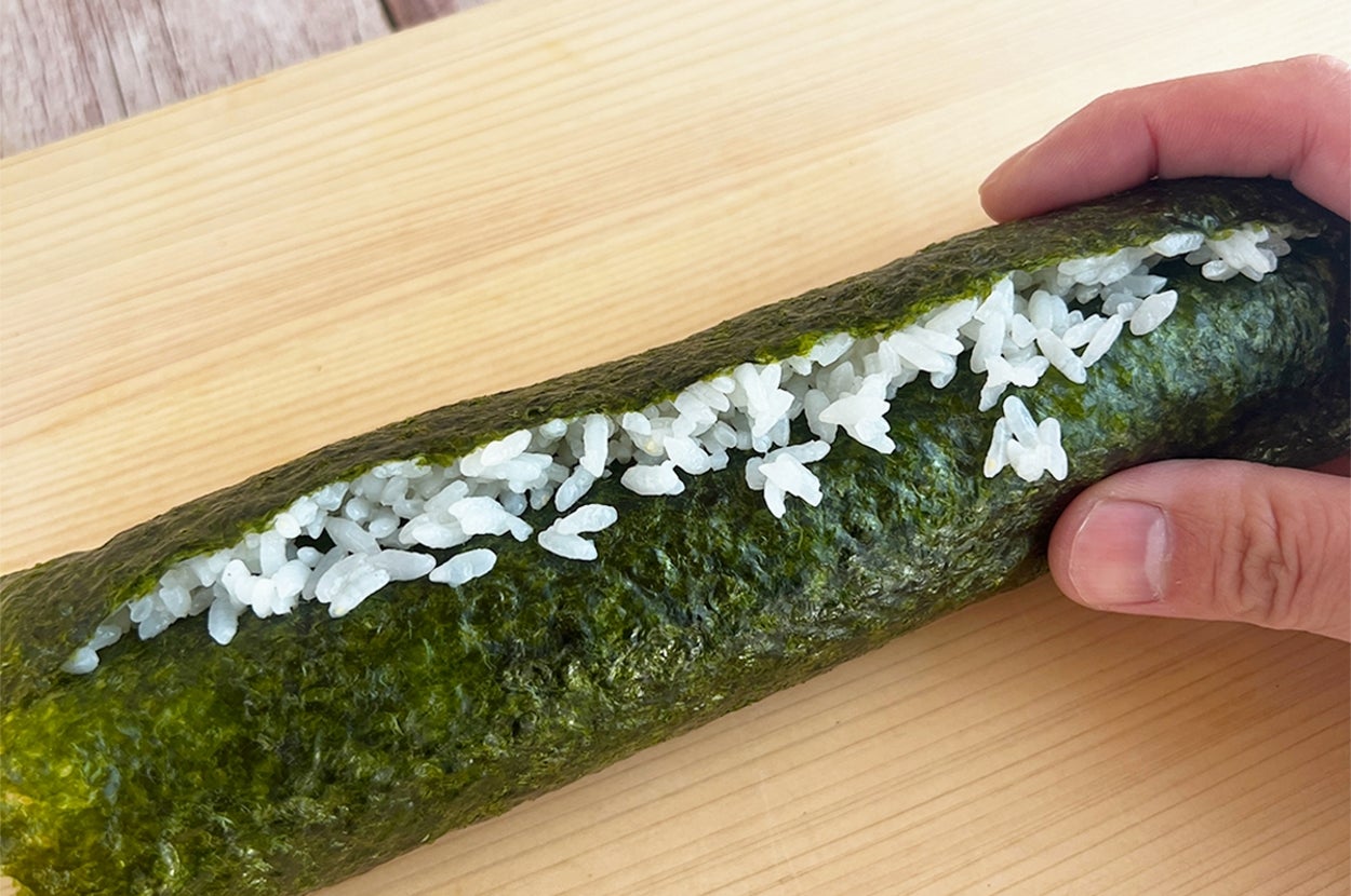 手巻き寿司を握る手。木製の板の上にご飯と海苔が巻かれている。
