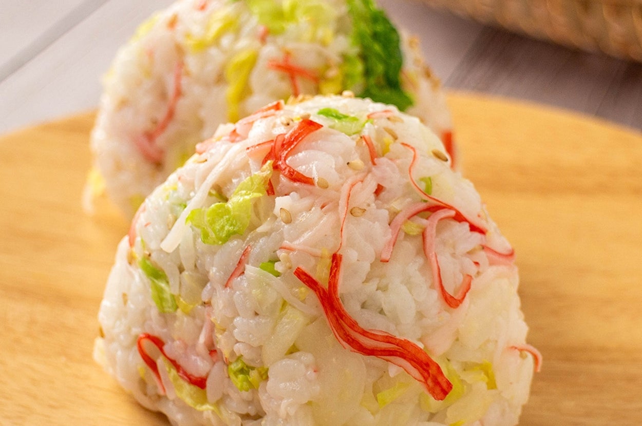 2つのカニカマと野菜を混ぜたおにぎりが木製の皿に載せられています。