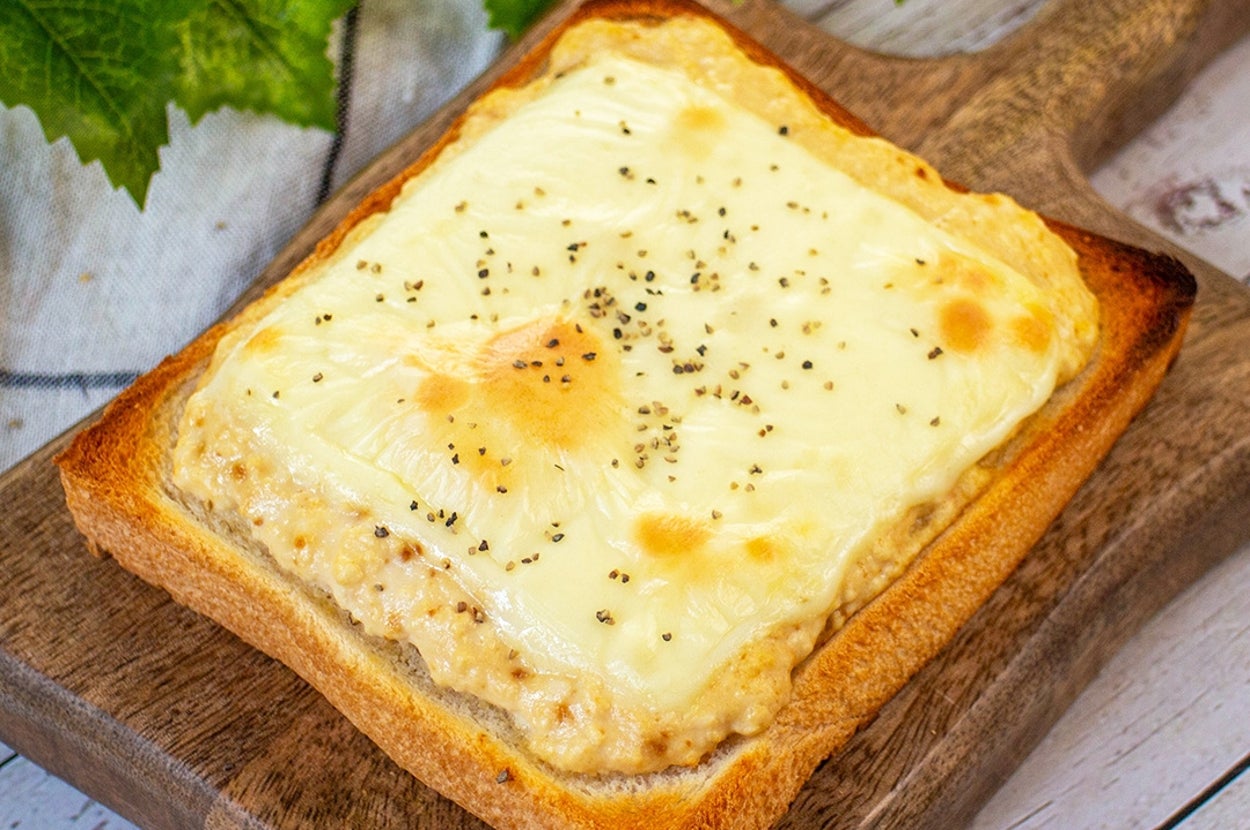 トーストにチーズが乗り、ペッパーが振りかけられています。木のプレートに置かれ、背後に緑の葉があります。