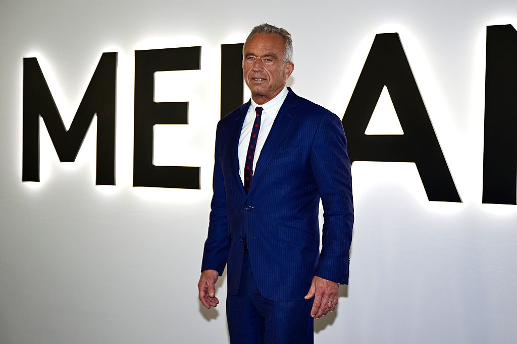 En person i blå dress med slips står foran et stort, delvis synlig skilt på et arrangement