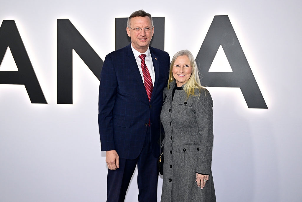 To personer poserer sammen på en rød løper. Man har på seg mørk dress og rødt slips; den andre har på seg en lang, grå frakk