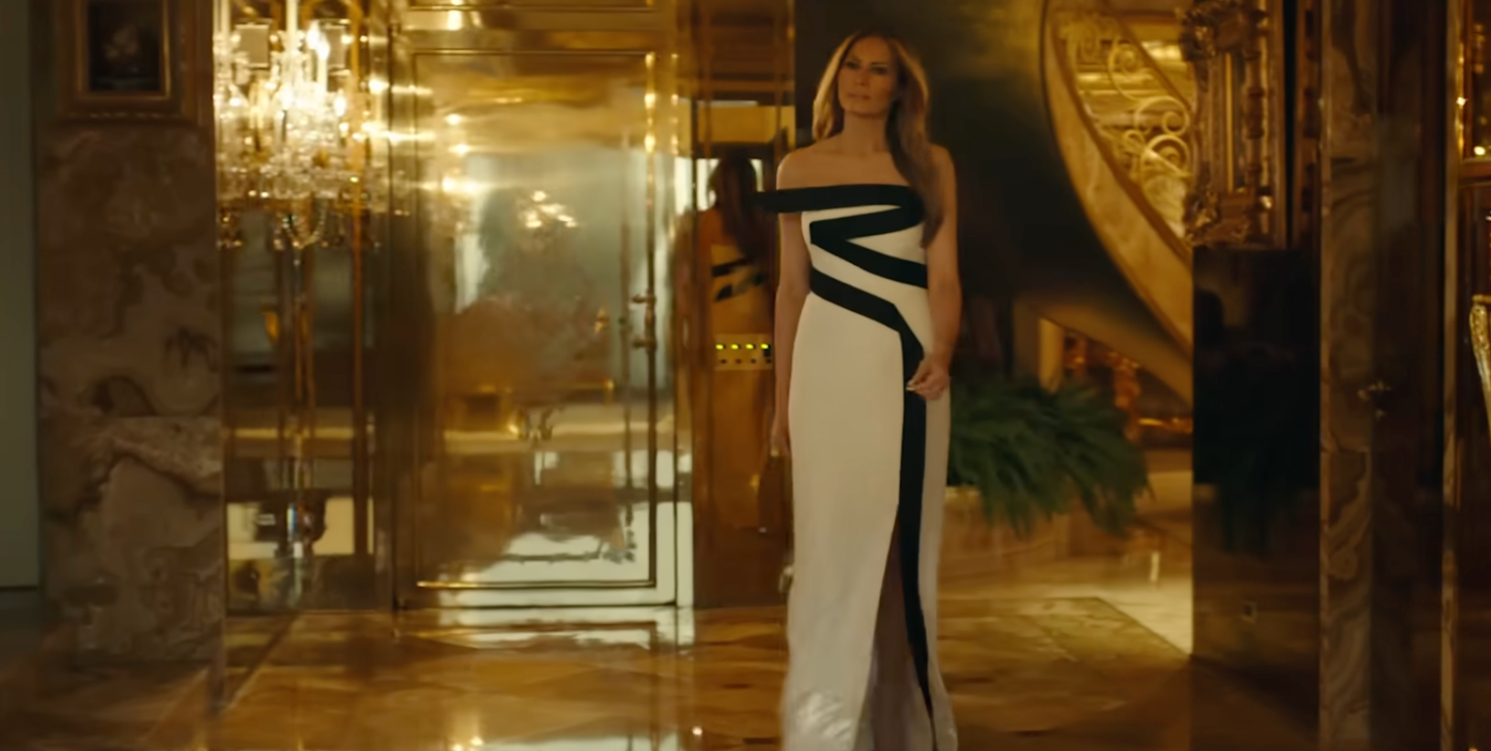 Person i en elegant, gulvlang, en-skulder kjole med dristig geometrisk design står i et luksuriøst interiør, muligens en gang eller foaje